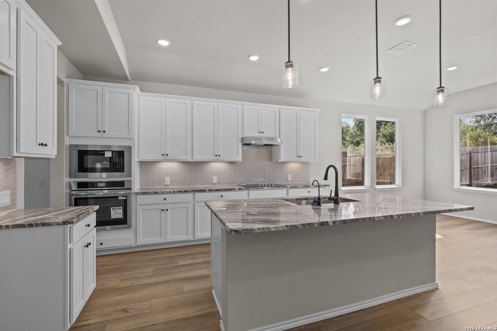 Modern white kitchen with granite island, stainless appliances, and pendant lights in Davidson Homes Sequoia C, San Antonio