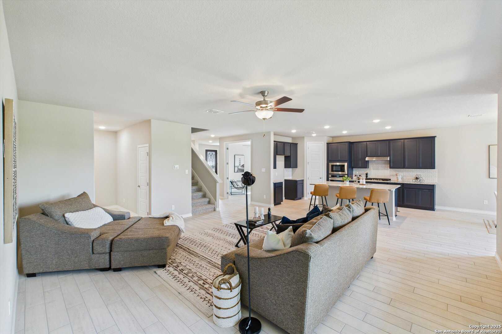 Spacious open living room with gray sectional sofa, ceiling fan, and modern kitchen island in Davidson Homes The Jennings H, Ladera, San Antonio
