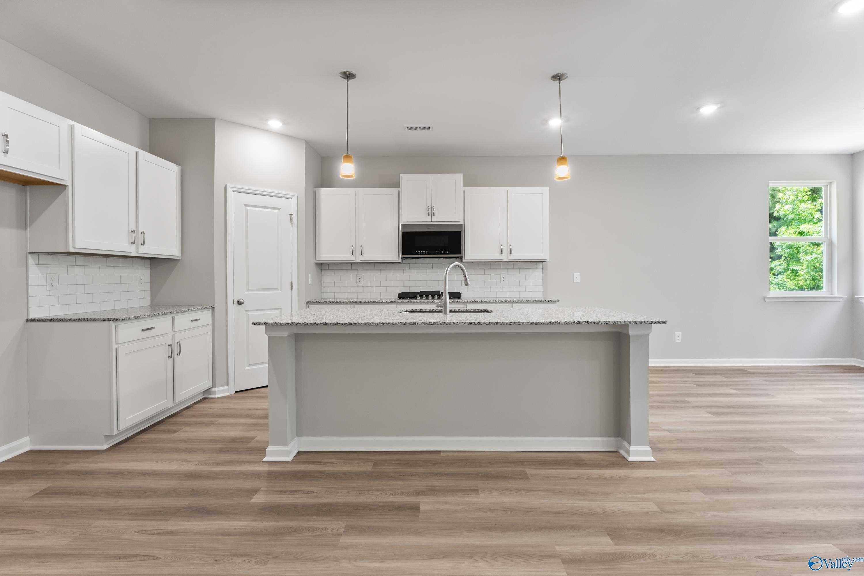 Modern white kitchen with granite island, subway tile backsplash, stainless appliances in Davidson Homes The Phoenix, Hazel Green, AL