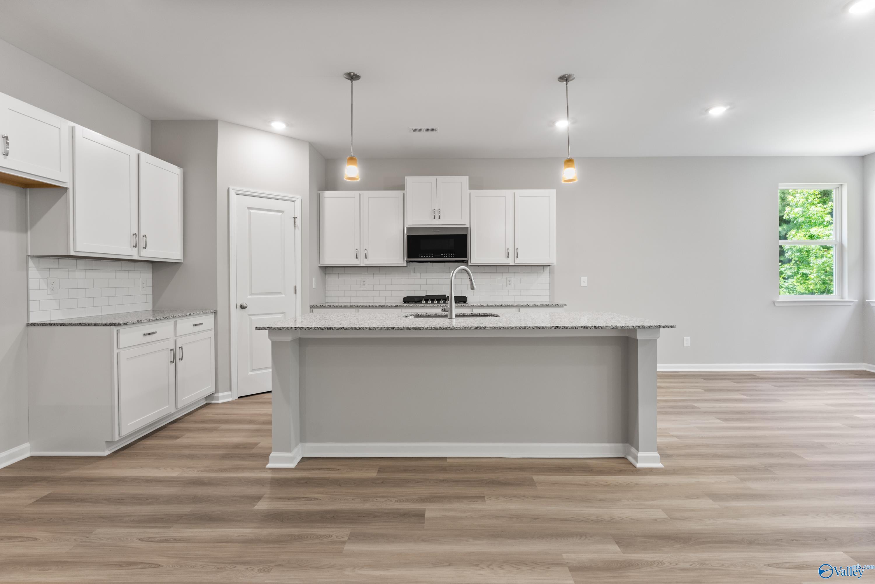 Modern white kitchen with large gray island, stainless appliances, subway tile backsplash in The Phoenix 3-bedroom home, Hazel Green, AL