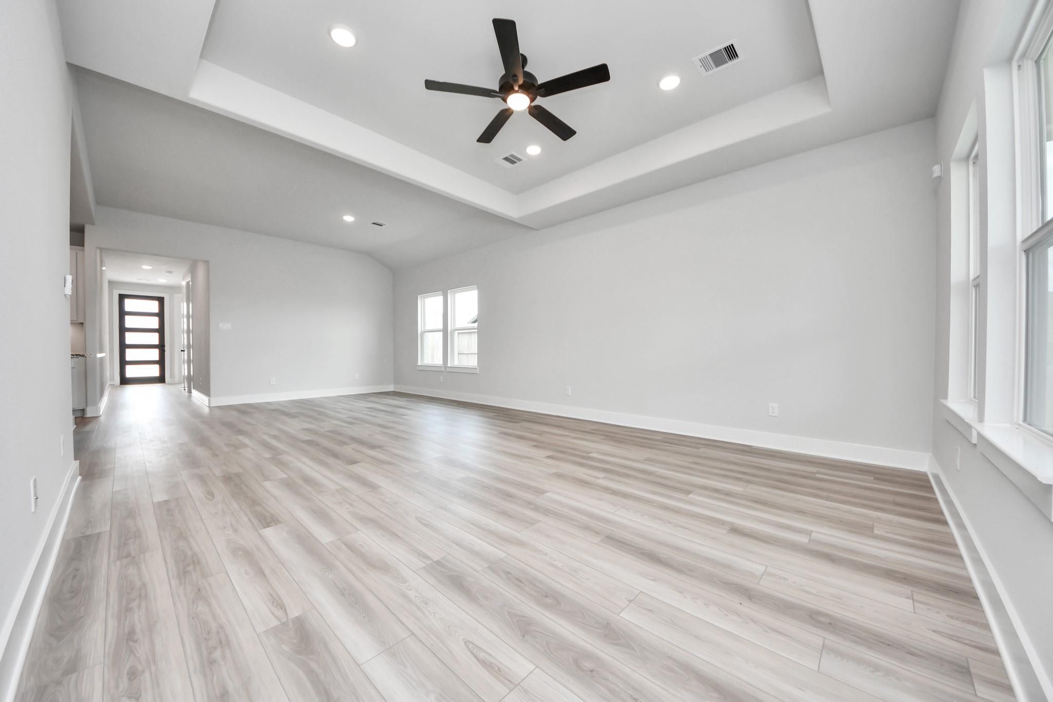 Spacious living room with tray ceiling and wood-look flooring in The Laguna C floor plan by Davidson Homes in Sunterra, Katy.