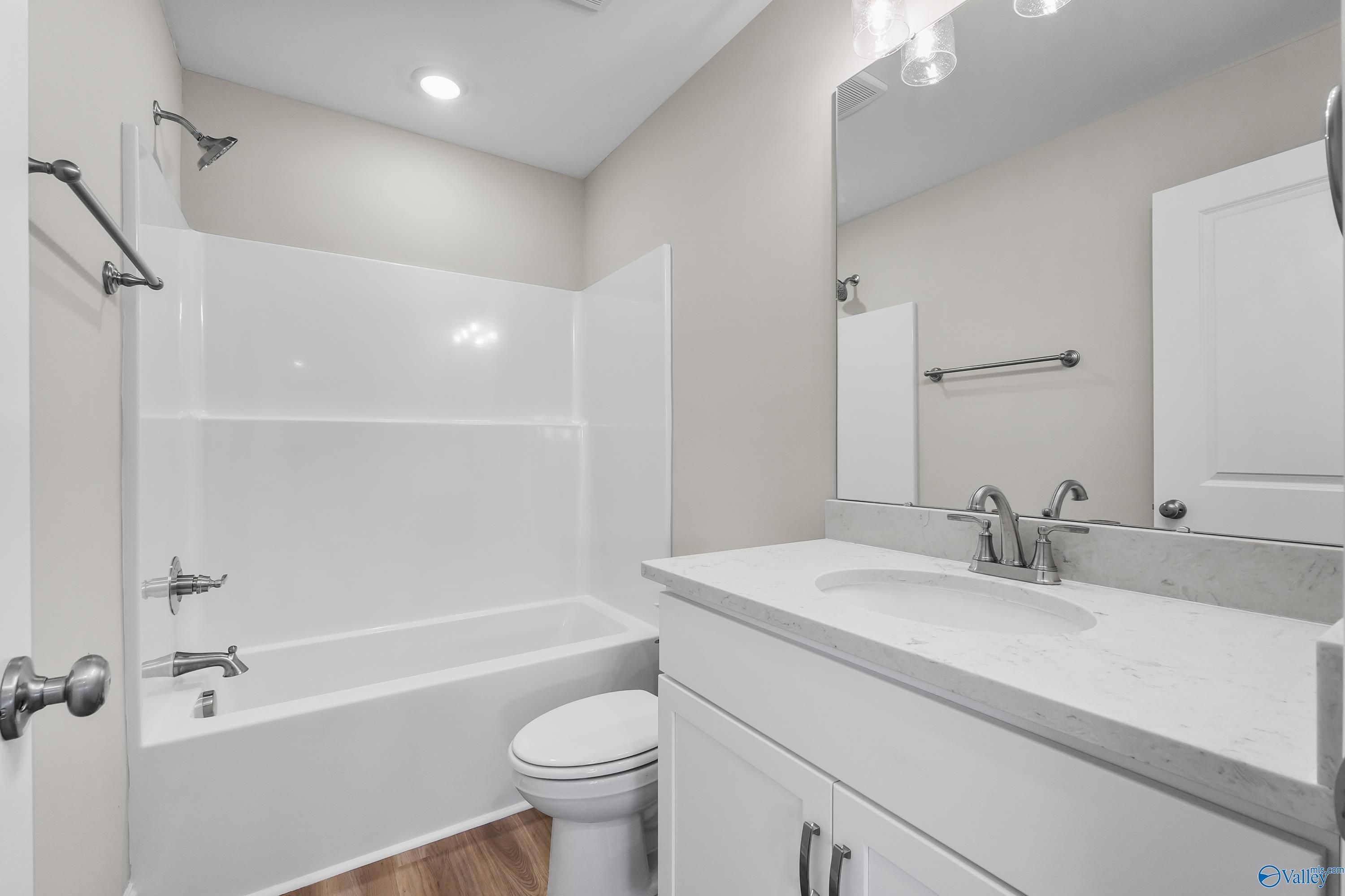 Bright bathroom with white tub-shower combo, quartz vanity, and toilet in Evermore Homes The Haven, Owens Cross Roads, Alabama