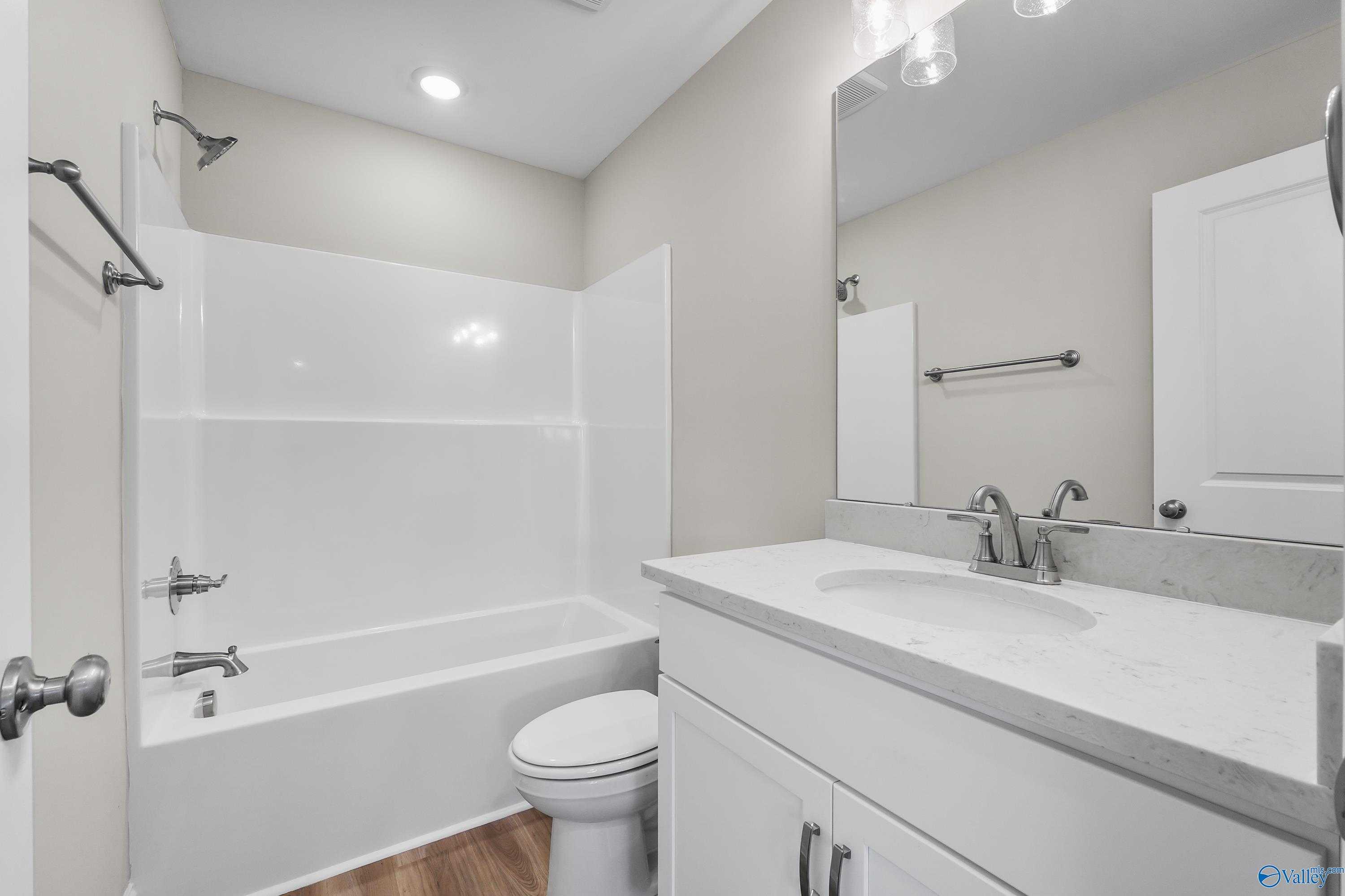 Bright bathroom with white tub-shower combo, quartz vanity, and toilet in Evermore Homes The Haven, Owens Cross Roads, Alabama