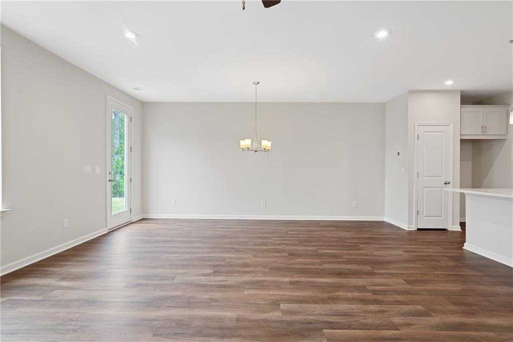 Spacious open living room with ceiling fan, chandelier, luxury vinyl plank flooring, and adjacent white kitchen in Davidson Homes Cary B, Kennesaw GA