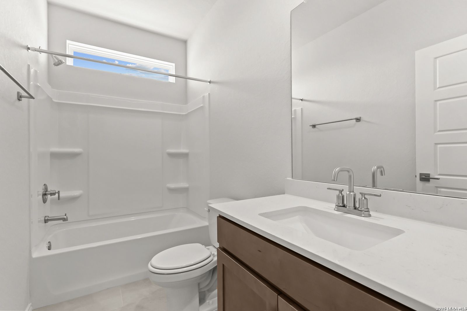 Bright white bathroom with tub shower combo, wood vanity, and quartz countertop in The Daphne I floor plan, Bricewood, San Antonio