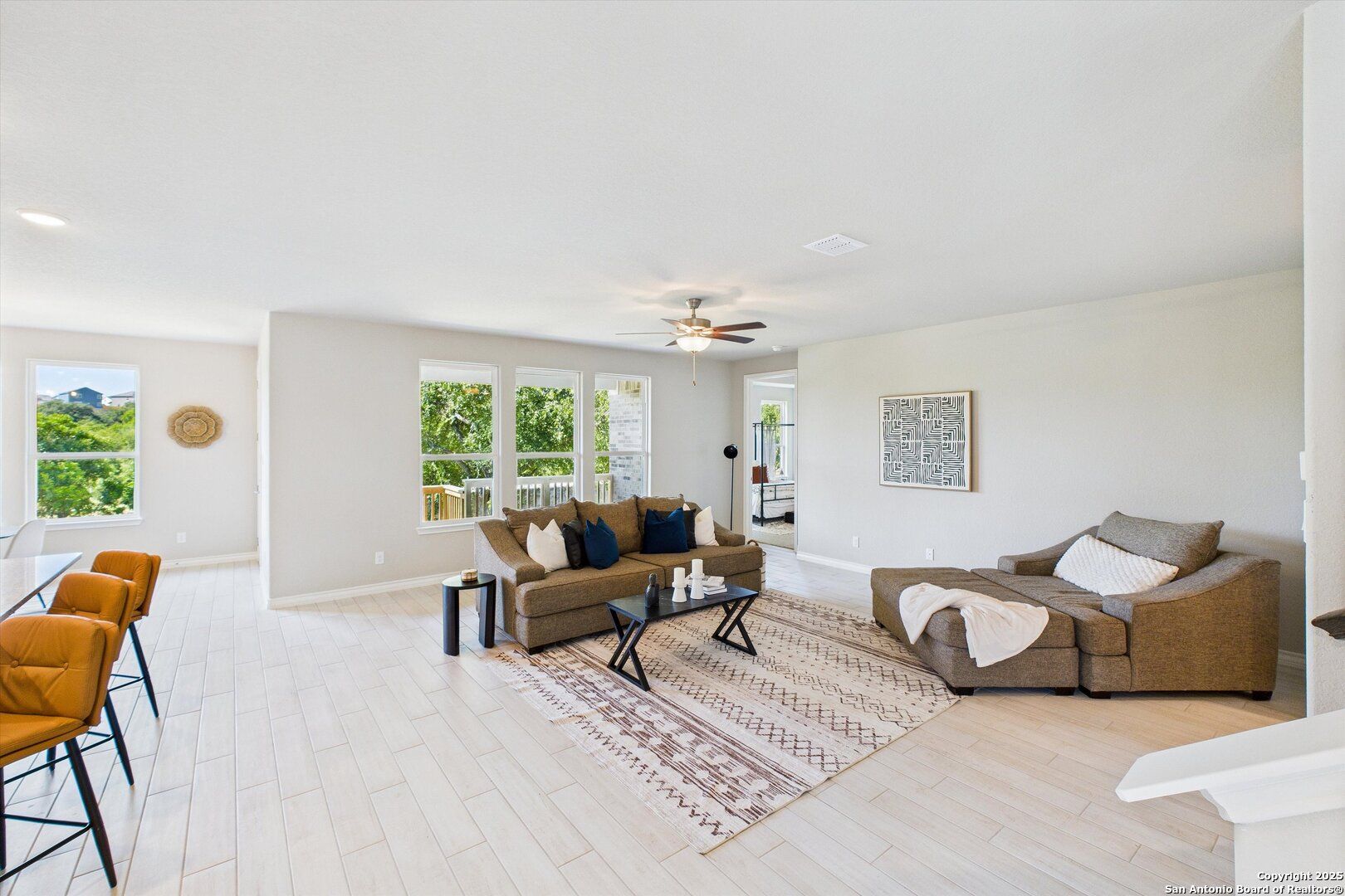 Bright open living room with large windows, neutral walls, brown sofa, ceiling fan, and rug in The Jennings H home, Ladera, San Antonio