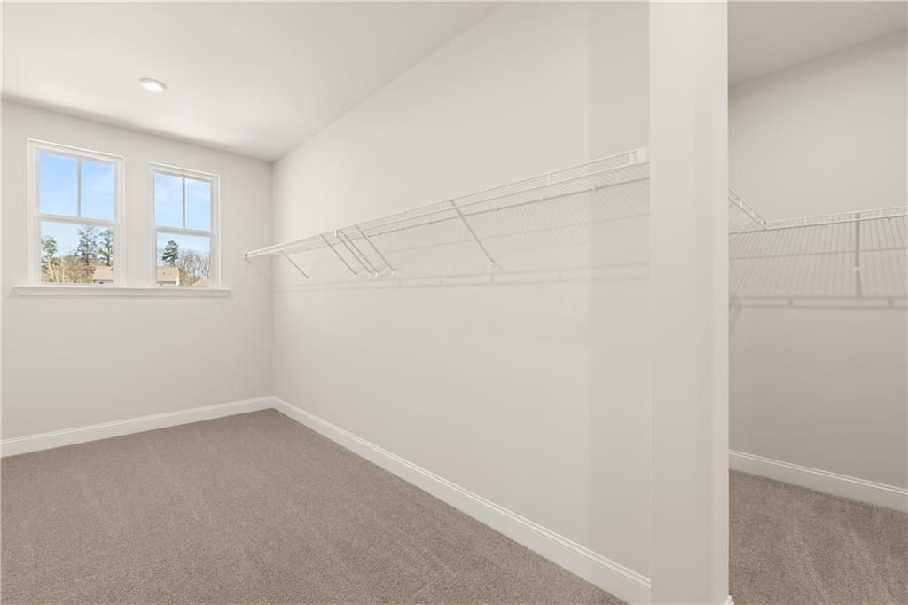 Spacious walk-in closet with white wire shelving, carpeted floor, and sunny windows in Davidson Homes The Danbury C, Buford, GA