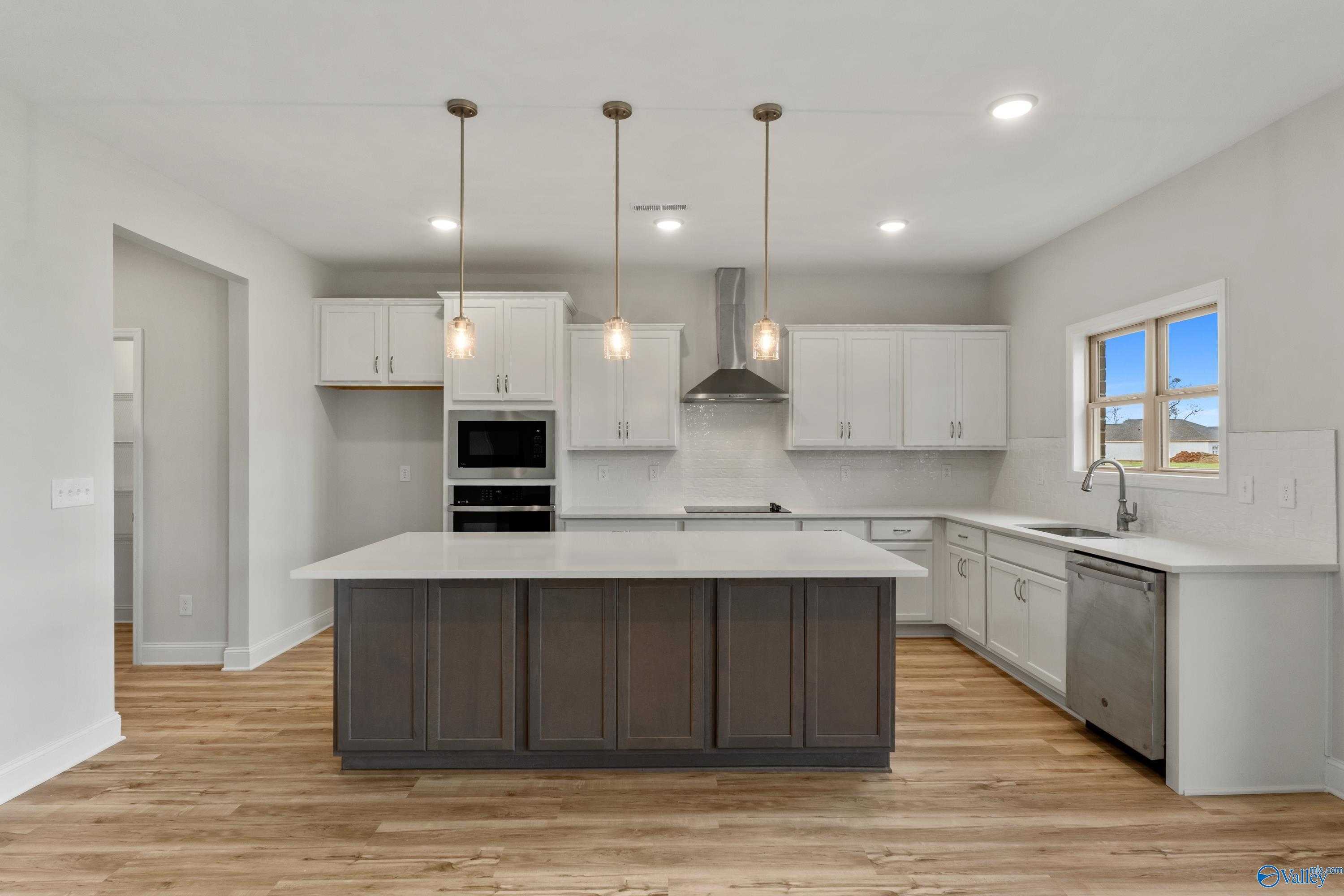 Modern kitchen with white shaker cabinets, gray quartz island, stainless double oven, and pendant lights in Davidson Homes Chelsea C, Harvest AL