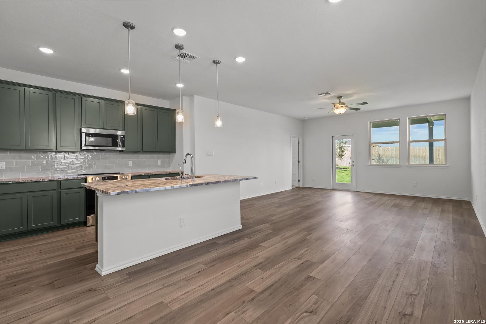 Open-concept kitchen with sage green cabinets and island in The Brazos B floor plan by Davidson Homes in Agave, San Antonio.