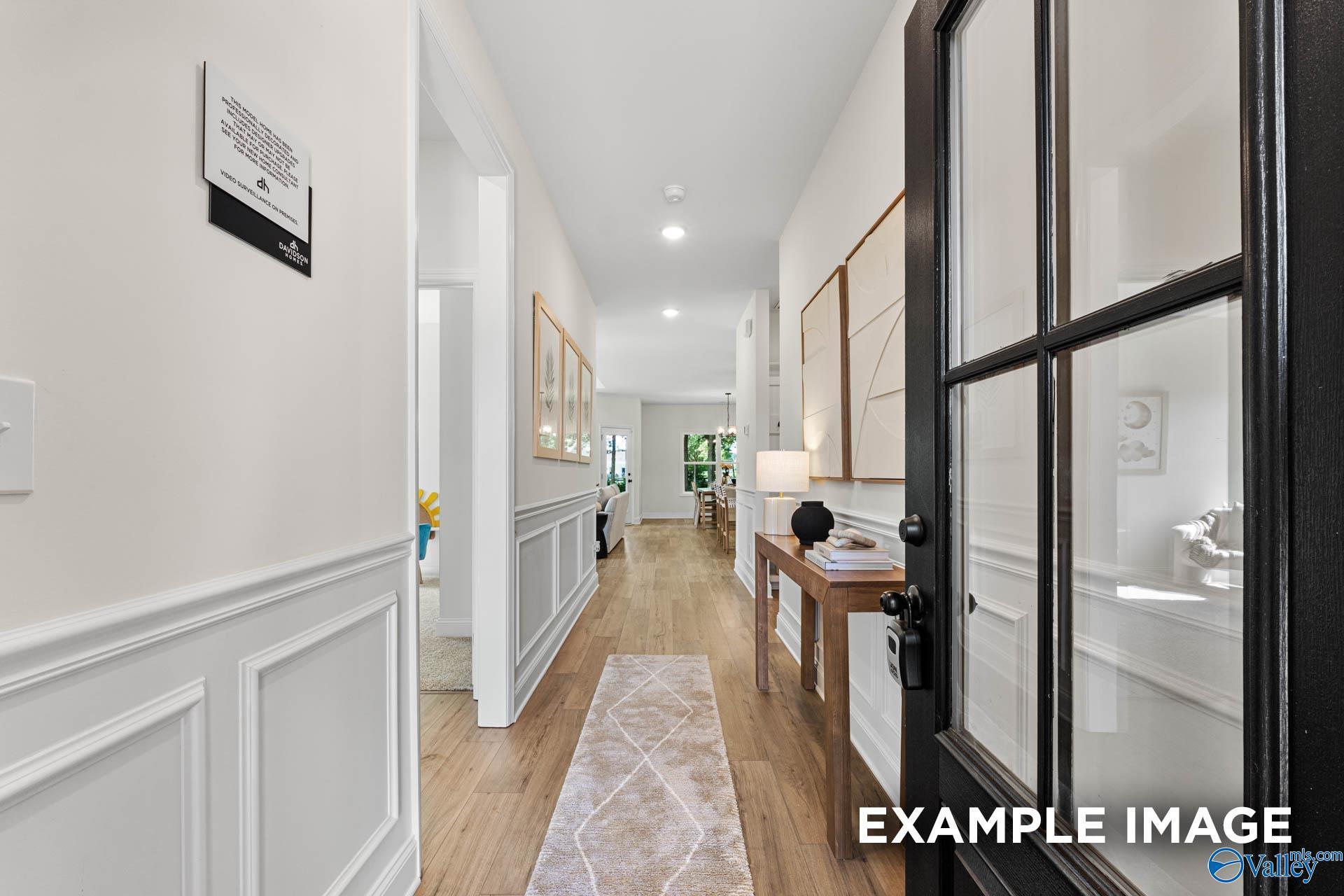 Bright hallway with wainscoted walls, hardwood floors, runner rug, and glass-paneled front door in Davidson Homes The Franklin, Huntsville