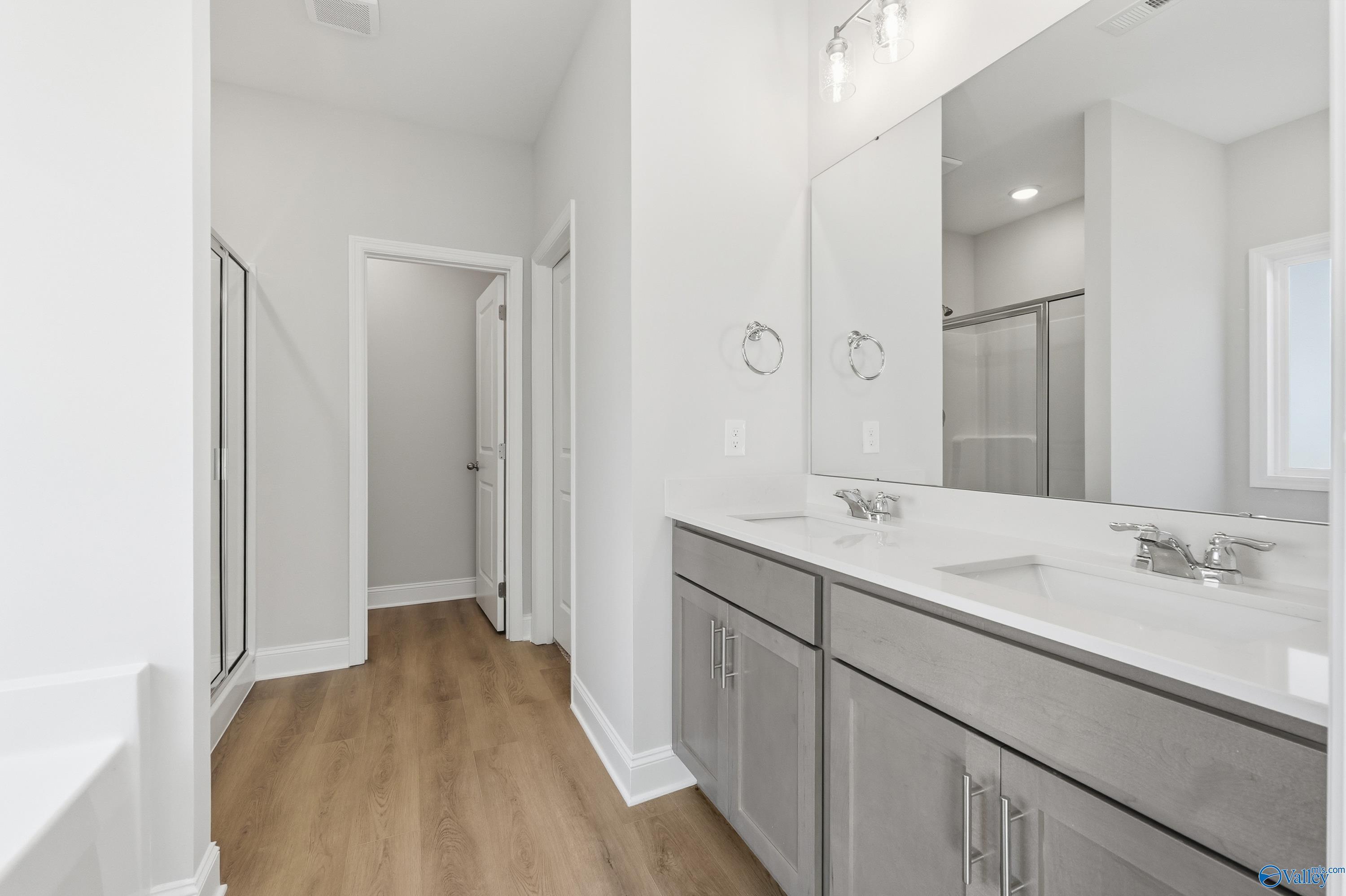 Modern double vanity with gray cabinets, large mirrors, and adjacent walk-in shower in The Daphne C by Davidson Homes, Arab, Alabama