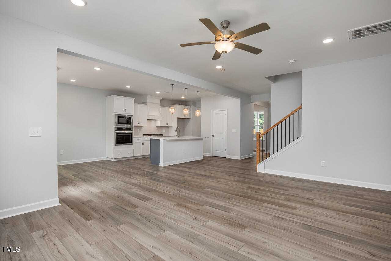 Open-concept kitchen and living area with white island, hardwood floors, ceiling fan, and staircase in Davidson Homes The Willow G, Wake Forest, NC