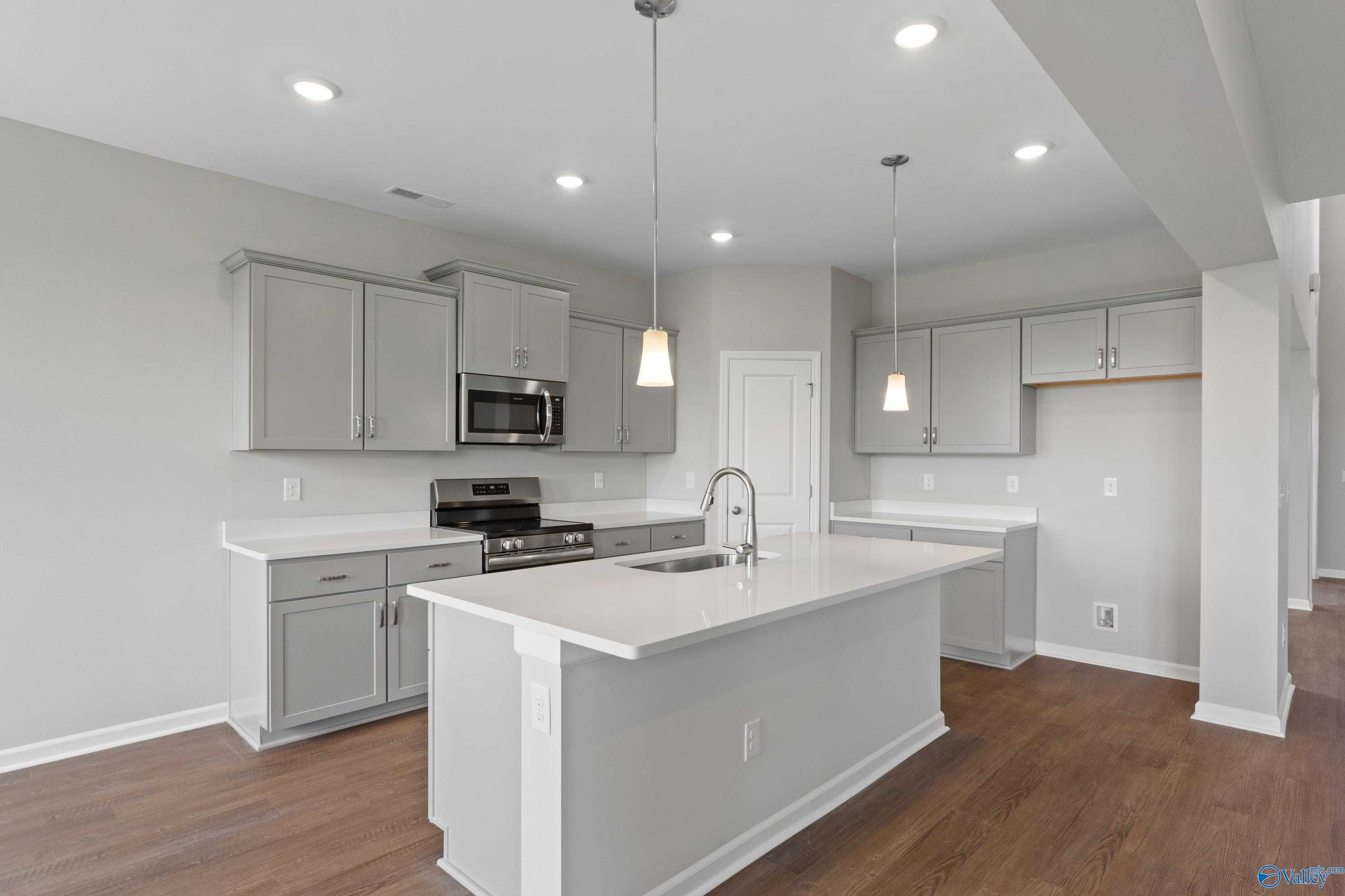 Modern gray kitchen with white quartz island, stainless appliances, pendant lights in Davidson Homes The Dorado, Athens AL
