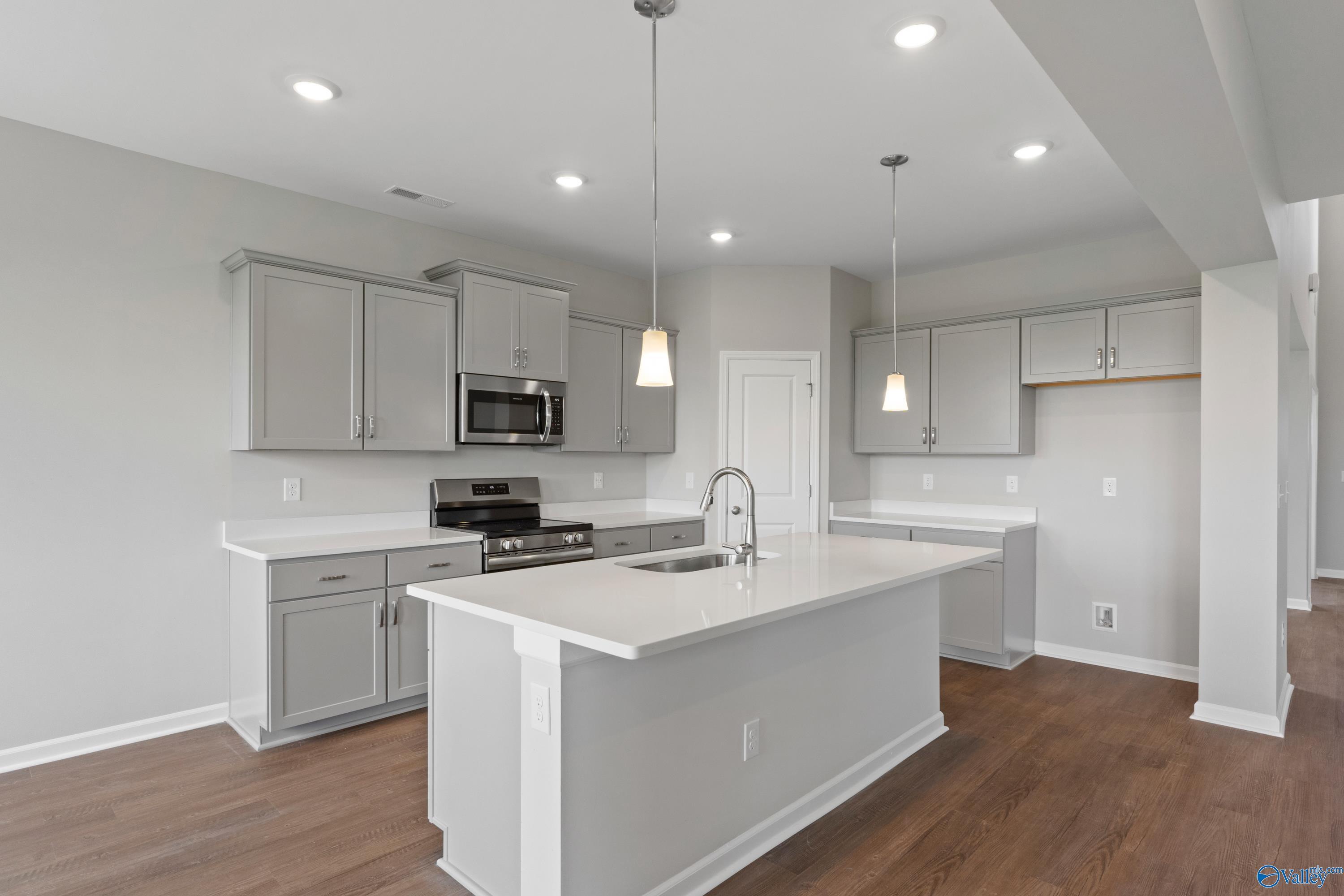 Modern gray kitchen with white quartz island, stainless appliances, pendant lights in Davidson Homes The Dorado, Athens AL