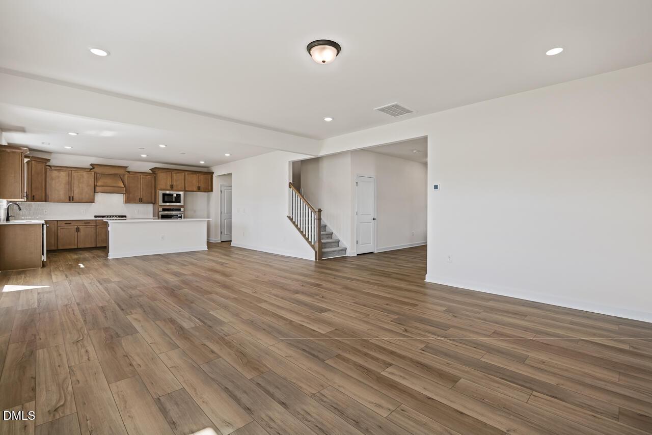 Open-concept living area with wood-look flooring, kitchen island, and staircase in Davidson Homes The Hickory II B, Lillington, NC