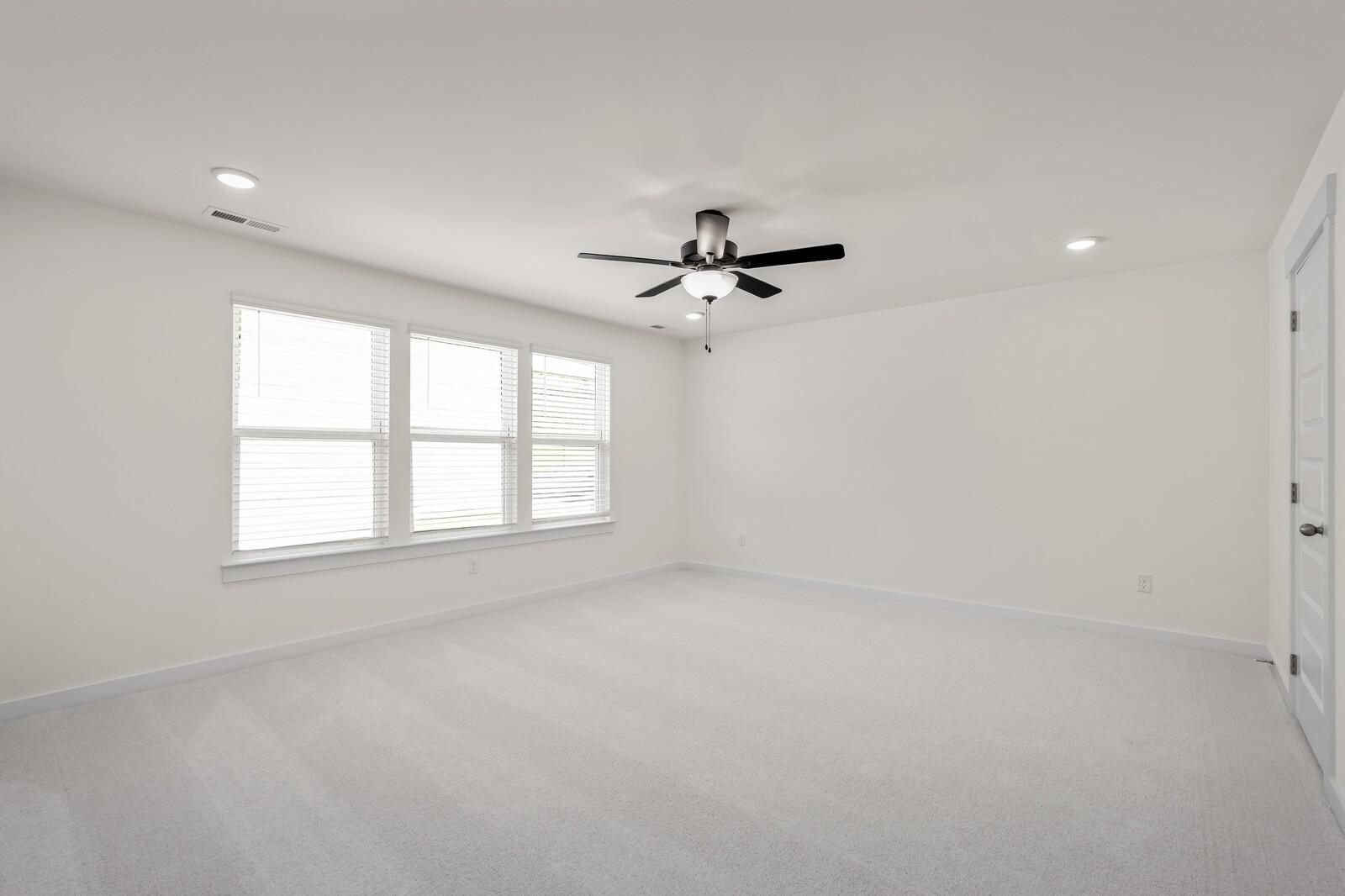 Spacious bedroom with neutral carpet and ceiling fan in The Willow floor plan by Davidson Homes in Woods Crossing, Gallatin.