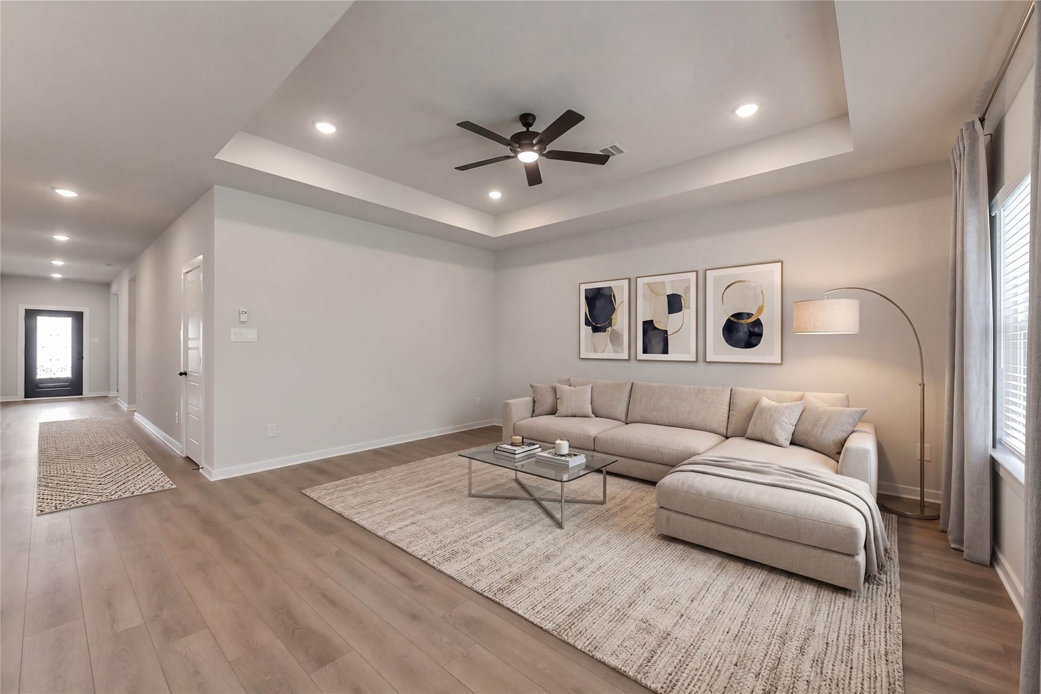 Spacious living room with L-shaped beige sofa, abstract art, ceiling fan, and hardwood floors in Davidson Homes Everett C, Crosby, Texas