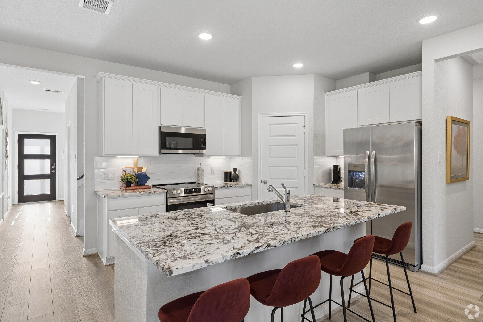 Modern kitchen at Liberty Estates in Cleveland TX with white cabinets, granite island, red bar stools, stainless appliances and hardwood floors