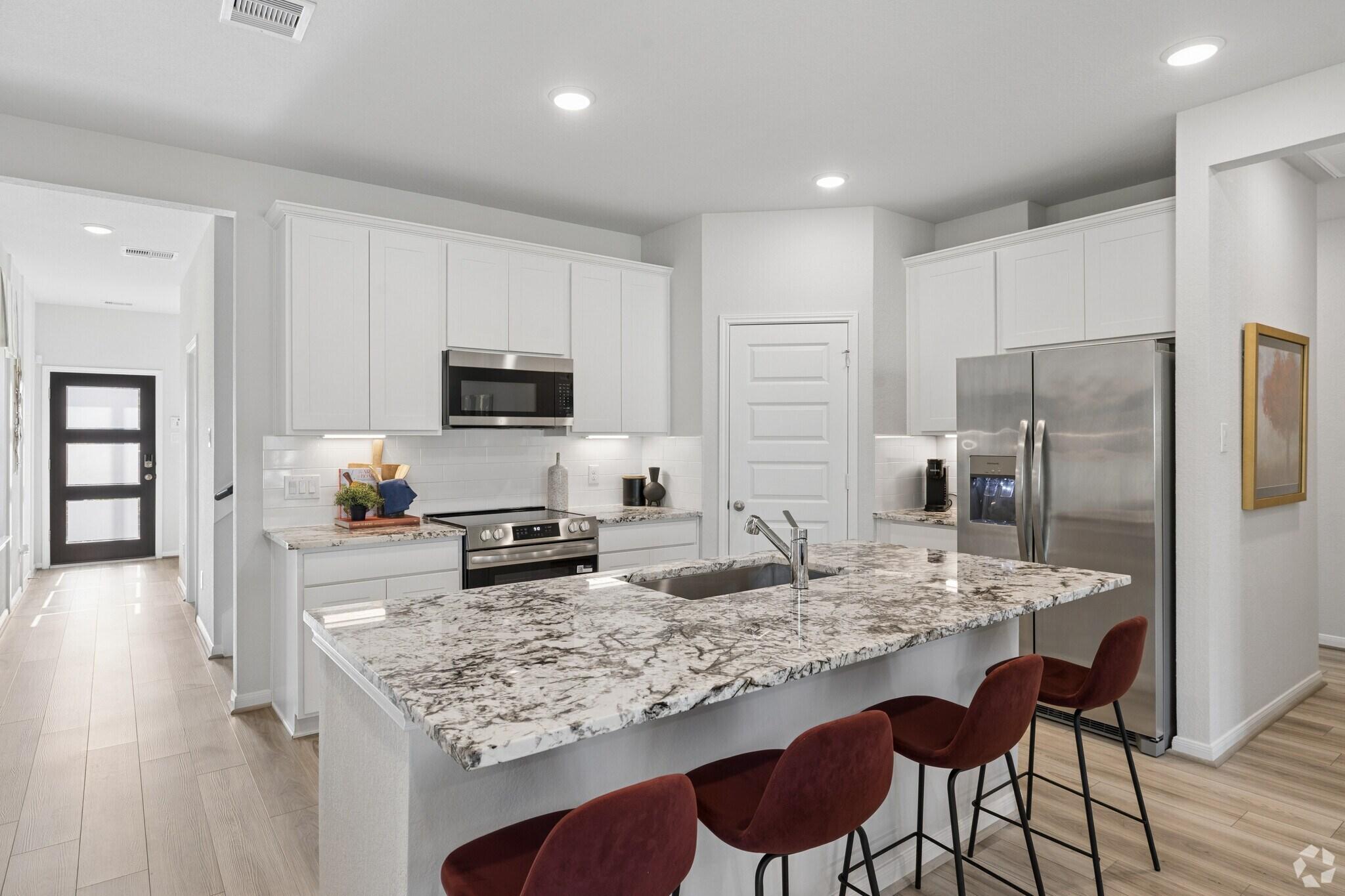 Modern kitchen at Liberty Estates in Cleveland TX with white cabinets, granite island, red bar stools, stainless appliances and hardwood floors