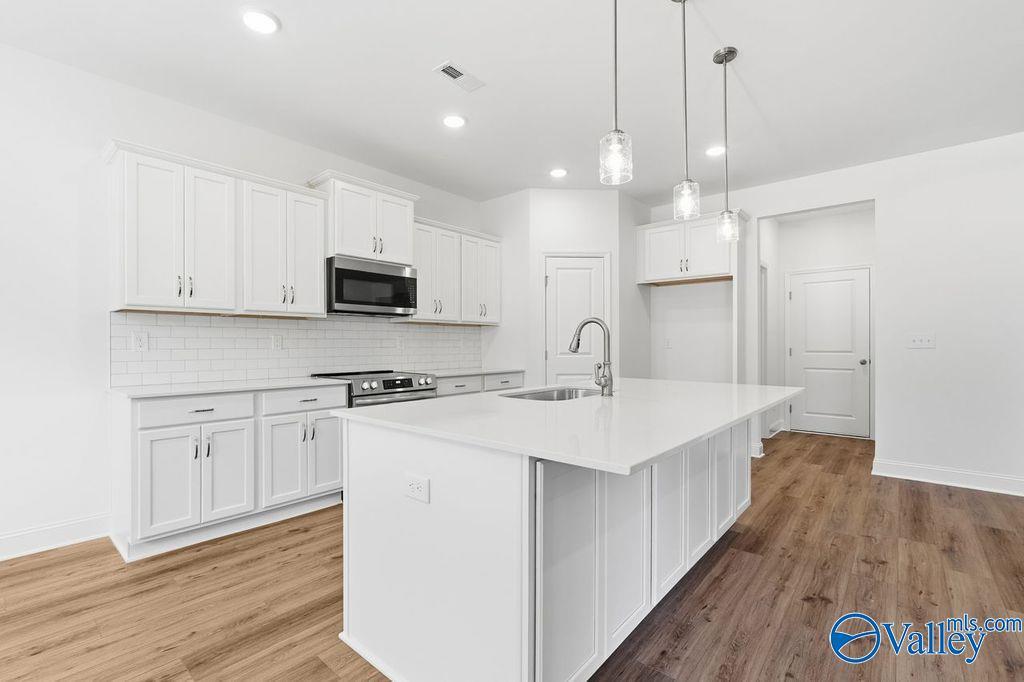 Modern white kitchen with quartz island, stainless appliances, subway tile backsplash in The Montgomery plan, Davidson Homes, Hartselle, AL