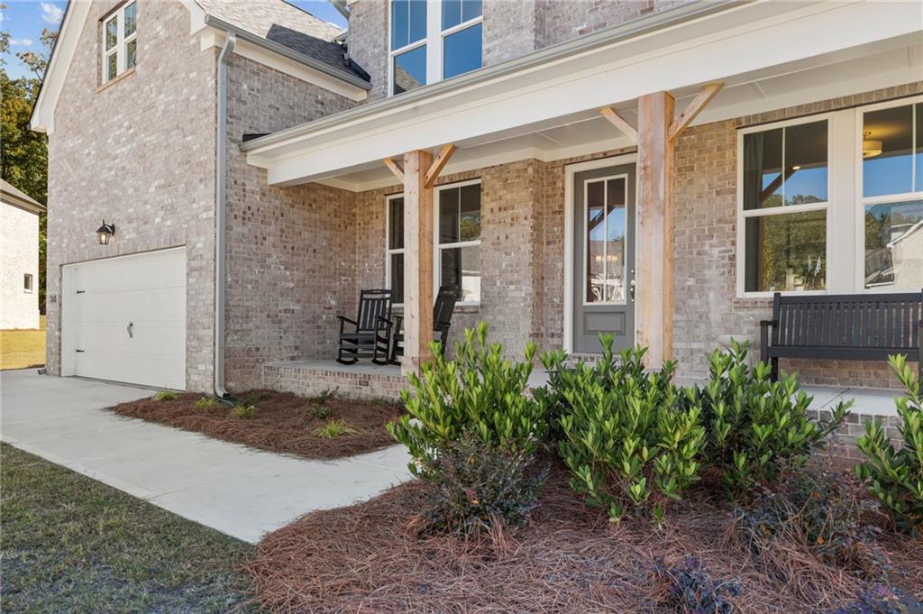 Modern brick 2-story Davidson Homes Danbury C with covered front porch, rocking chairs, 3-car garage, and landscaped entry in Buford, Georgia