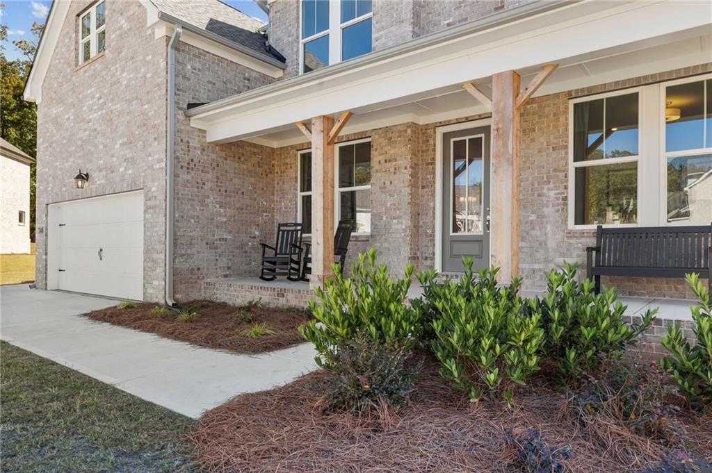 Modern brick 2-story Davidson Homes Danbury C with covered front porch, rocking chairs, 3-car garage, and landscaped entry in Buford, Georgia