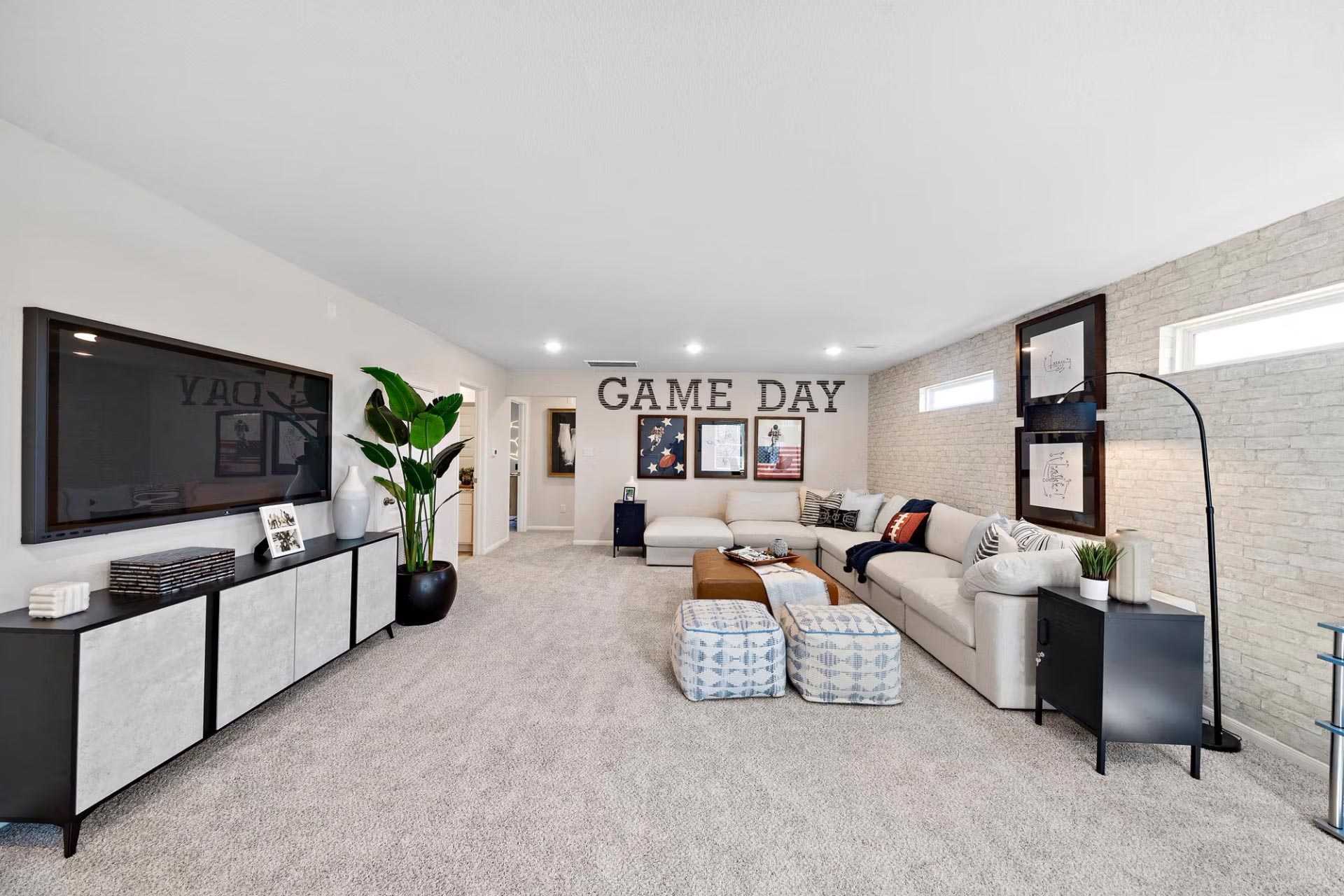 Spacious game room at Saddle Creek Ranch in Cibolo Texas with wall-mounted TV, white brick walls, sectional sofa, and GAME DAY decor