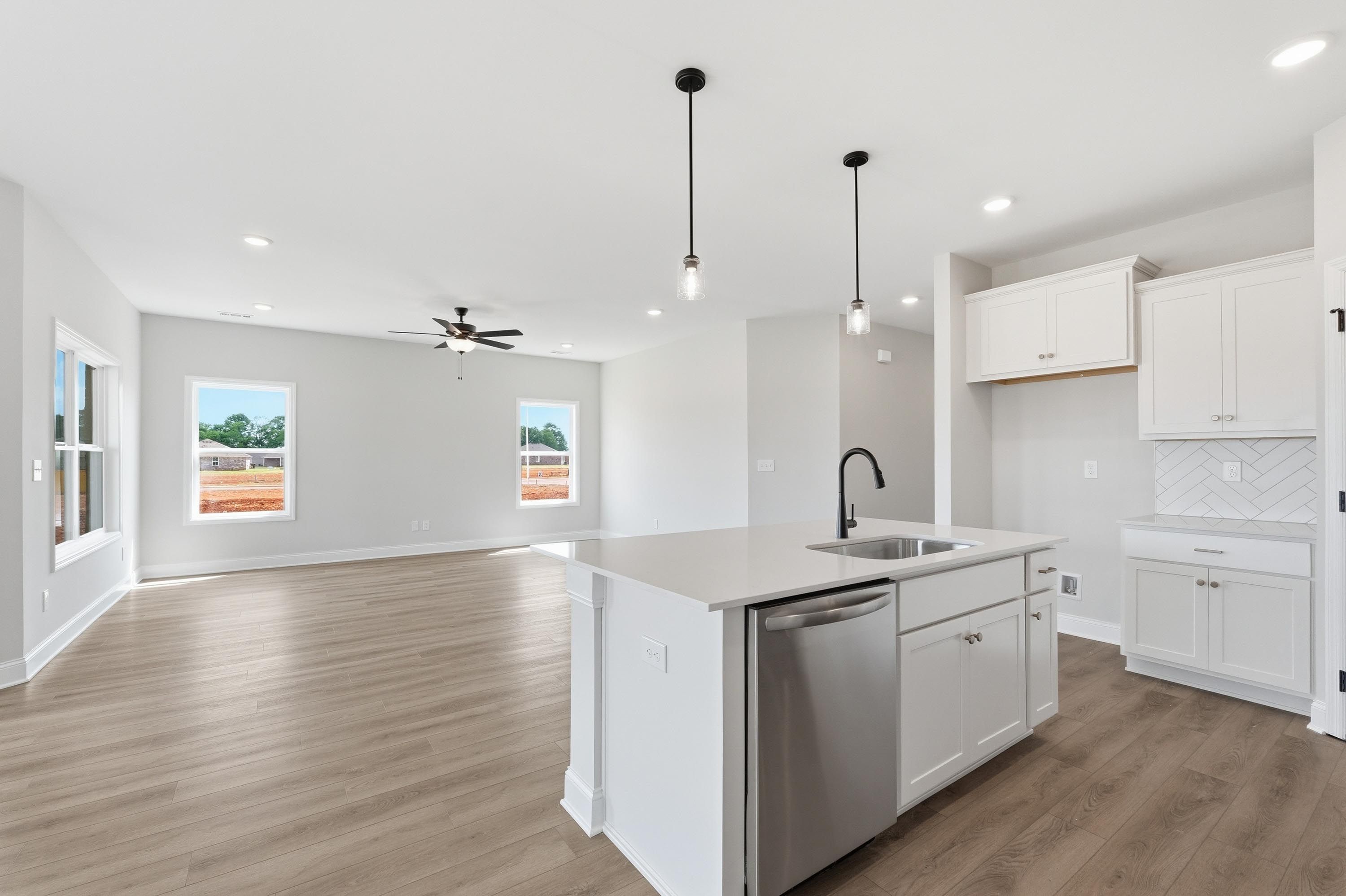 Open-concept kitchen and living area in The Glen A featuring a white island, modern cabinetry, and wood-style flooring.