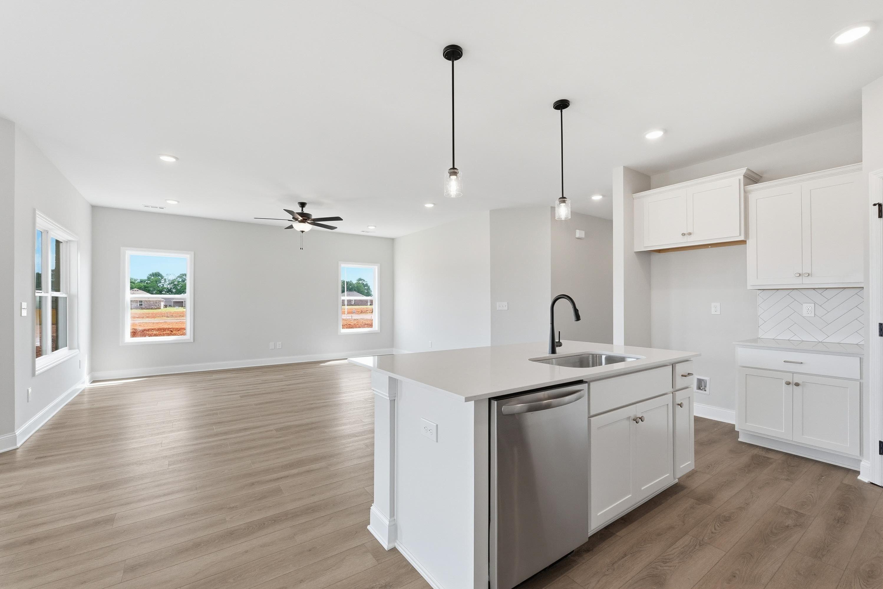 Open-concept kitchen and living area in The Glen A featuring a white island, modern cabinetry, and wood-style flooring.