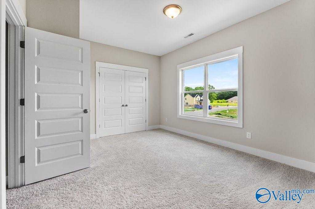 Bright bedroom with double closet doors and large window view of green yard in Evermore Homes The Oxford, Owens Cross Roads, AL