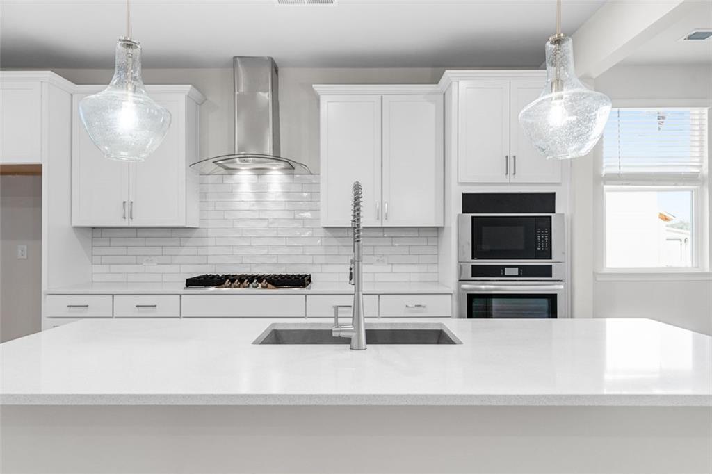 Modern white kitchen with quartz island, stainless sink, subway tile backsplash, and pendant lights in The Glenwood C at Wehunt Meadows, Hoschton