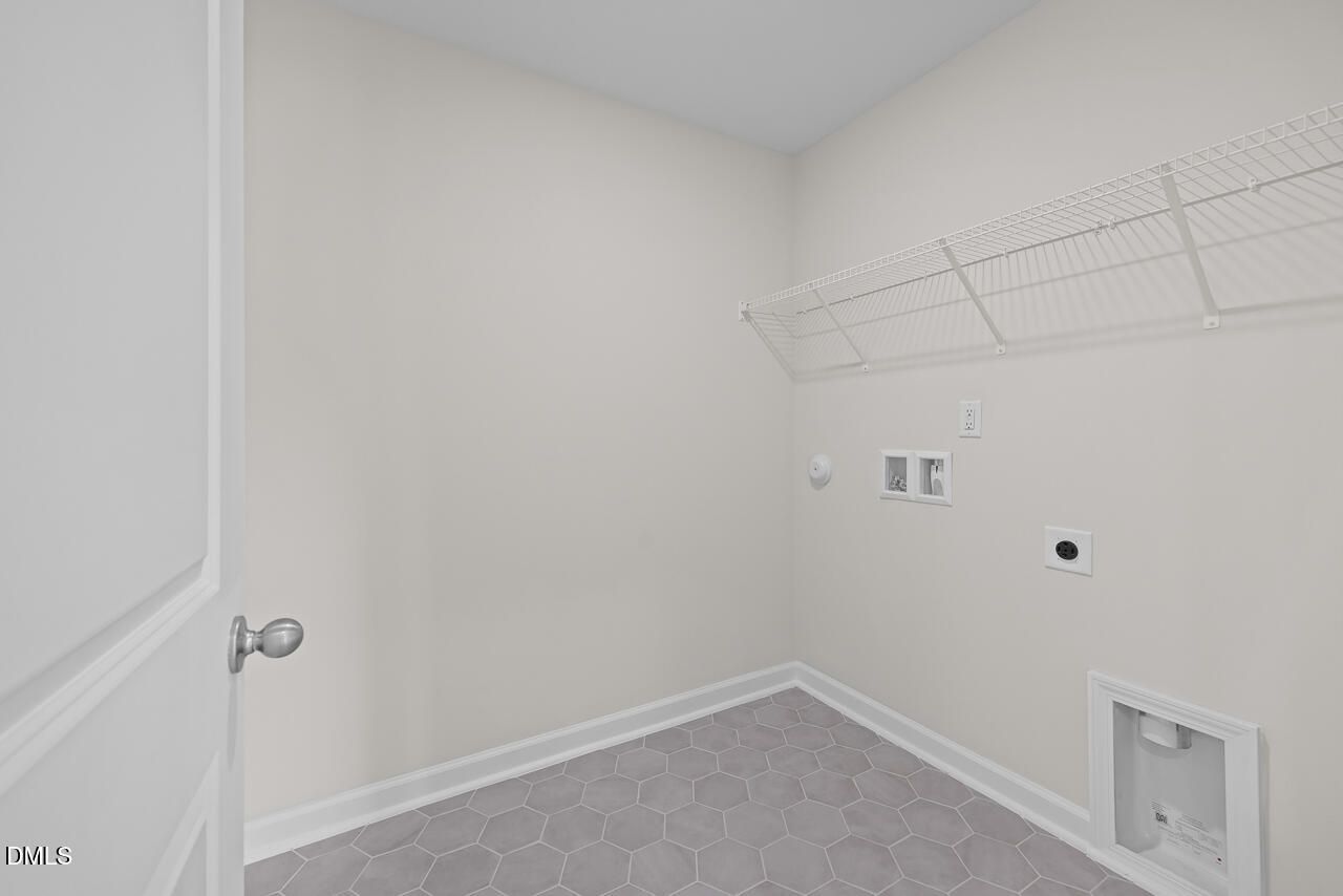 Laundry room with gray hexagon tile flooring, wire shelving, and washer connections in Davidson Homes The Mitchell plan, Knightdale NC