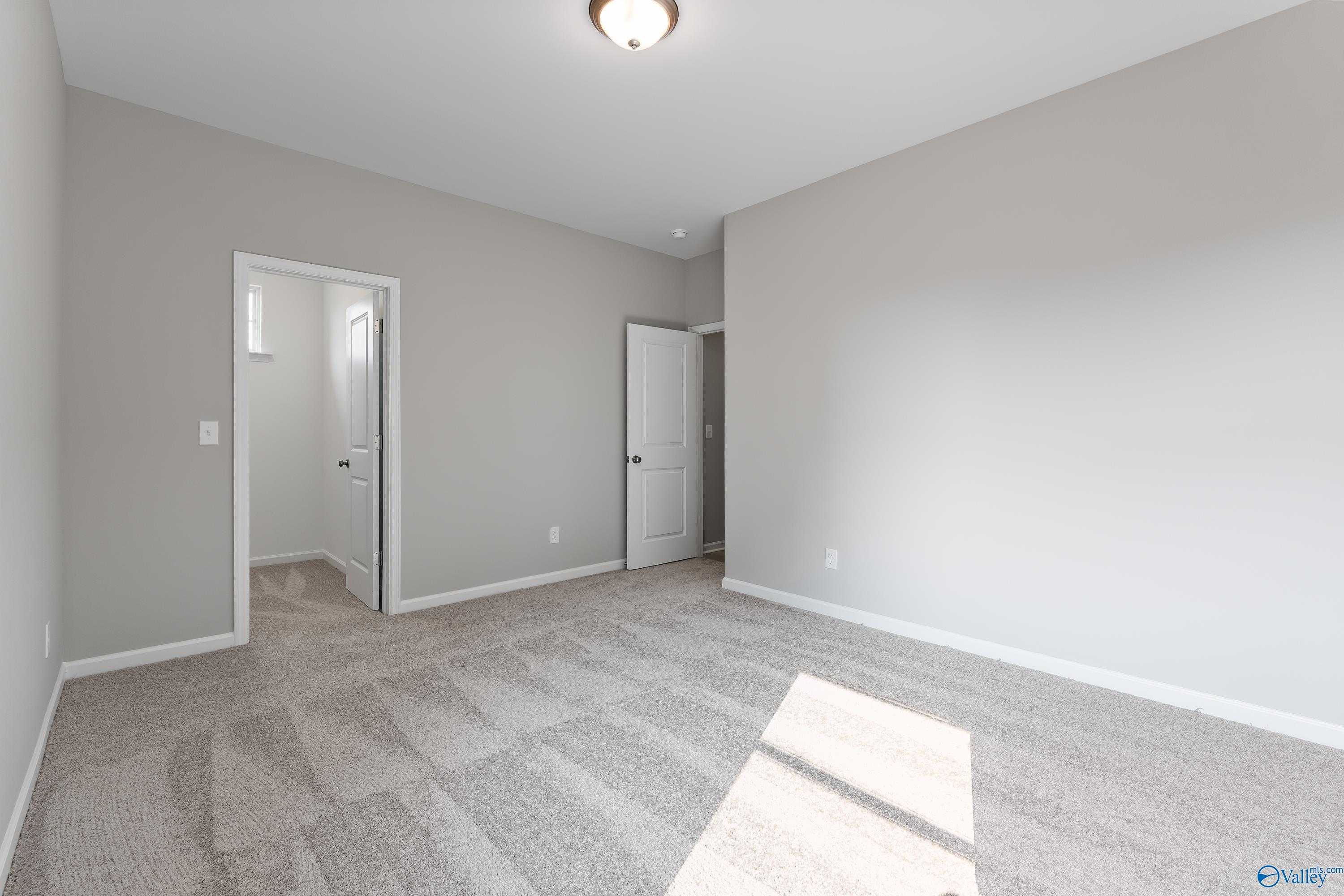 Spacious empty bedroom with light gray walls, carpet floor, and natural sunlight in Evermore Homes The Grace, Madison Alabama