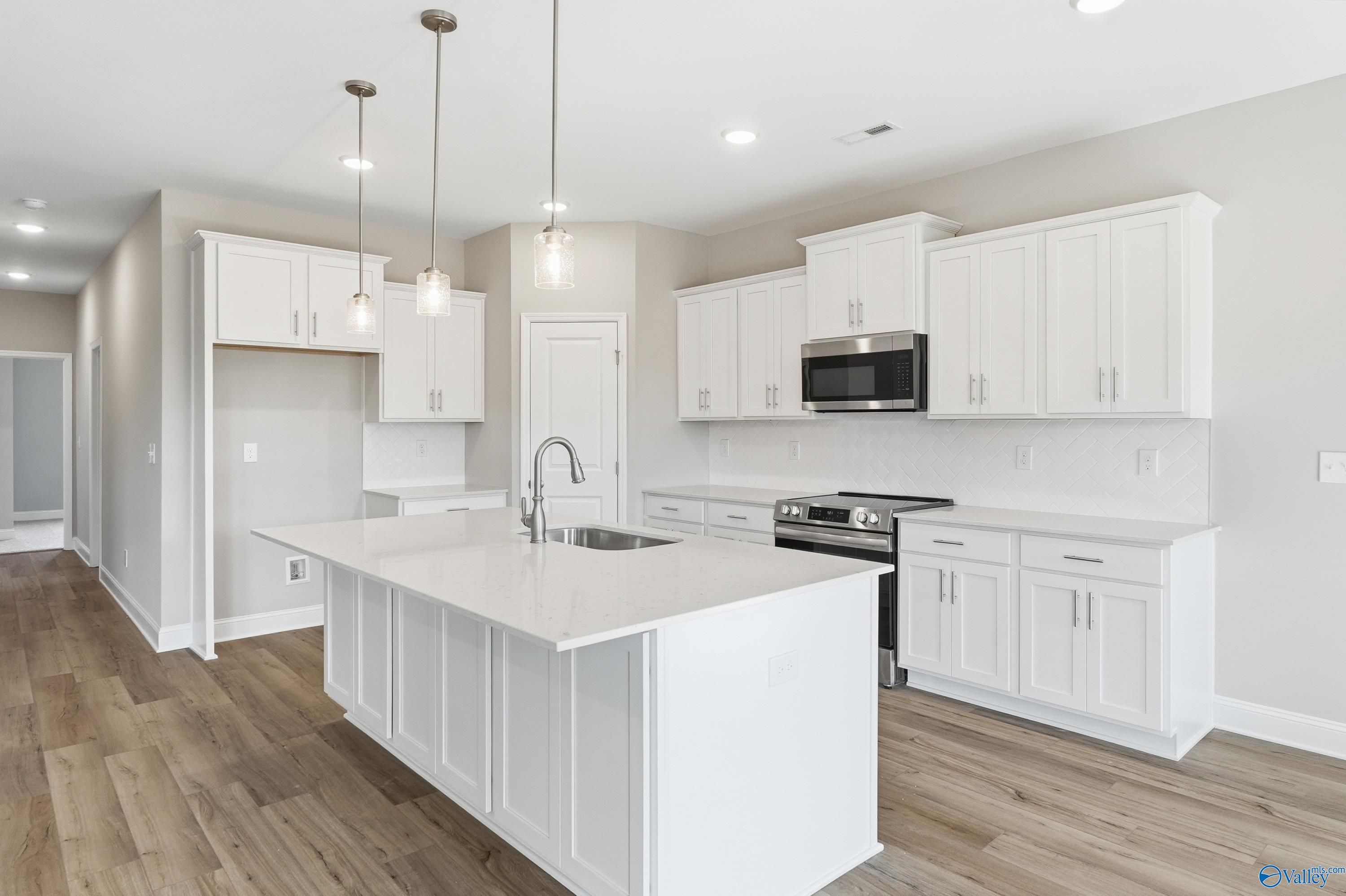 Modern white shaker kitchen with oversized island sink, stainless appliances, and pendant lights in Davidson Homes The Rockford, Harvest AL
