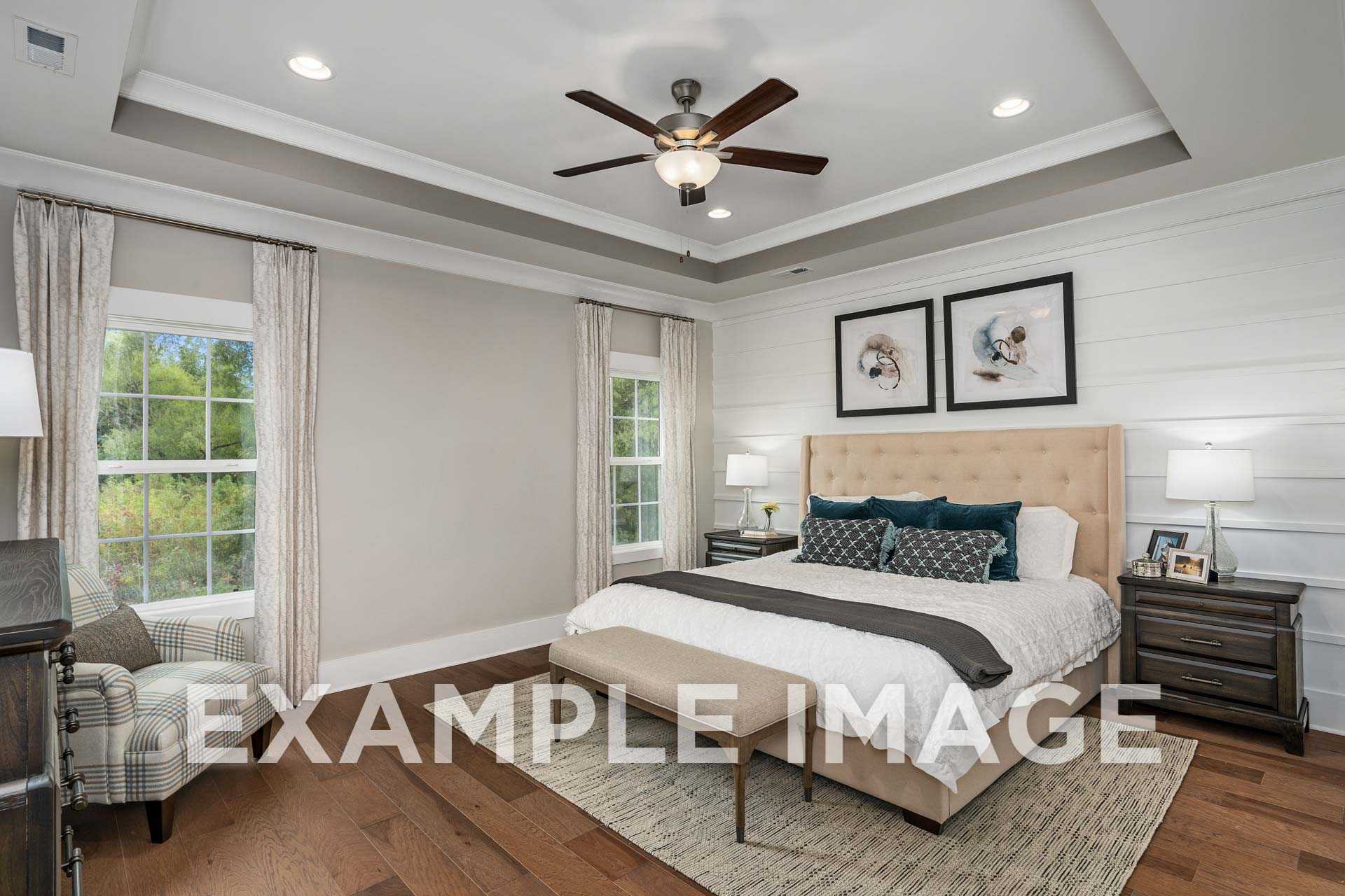 Spacious master bedroom in The Harrison featuring tufted upholstered bed, ceiling fan, large windows with sheer curtains, neutral tones, hardwood floors