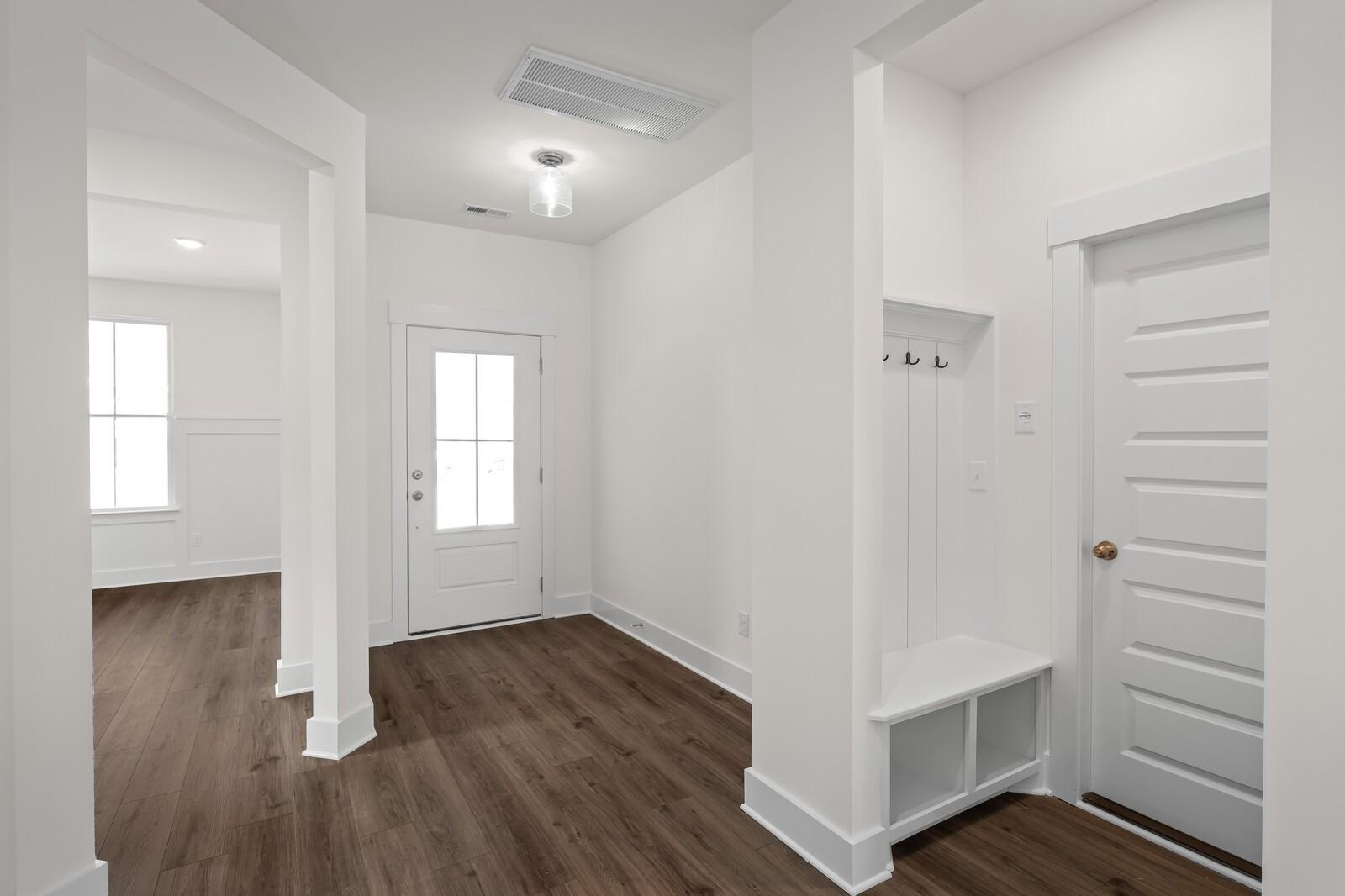 Bright entryway with built-in bench, coat hooks, hardwood floors and white arches in Davidson Homes The Ridgeport, Gallatin, TN