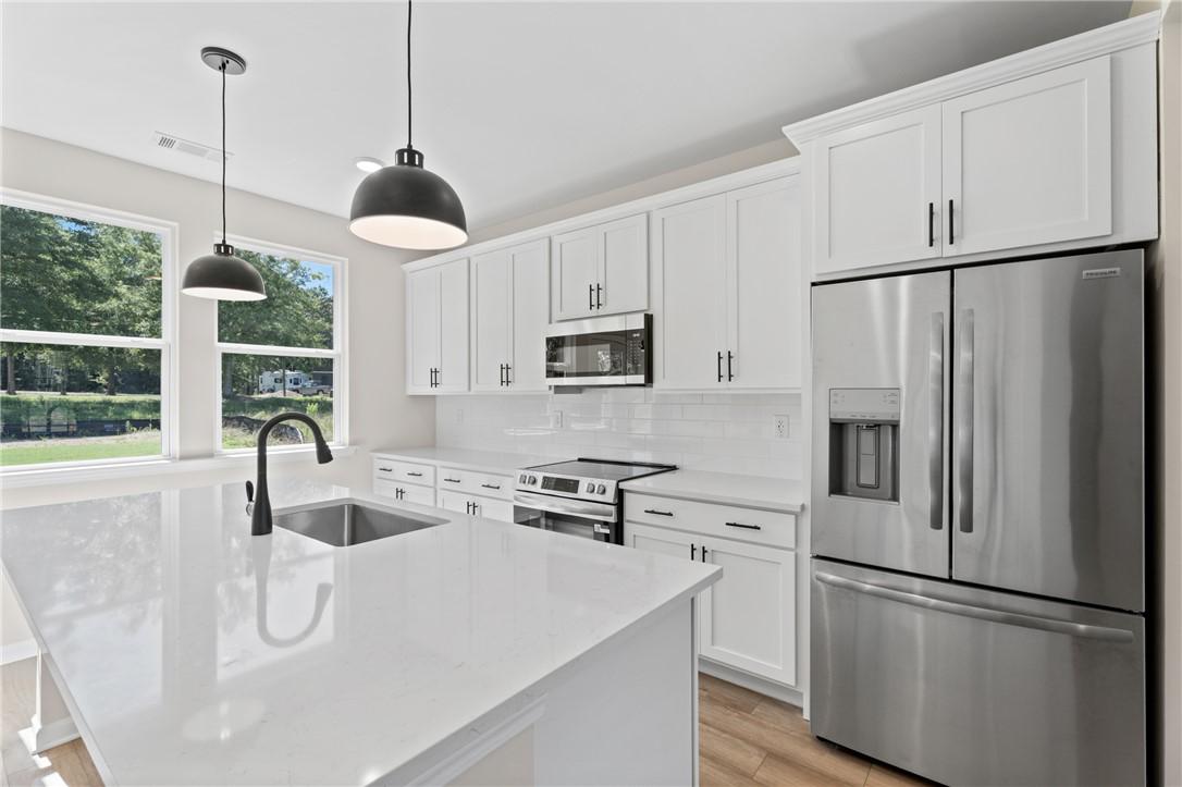 Modern kitchen with white cabinets, quartz island, and stainless appliances in The Stella C home, Links Crossing, Auburn.