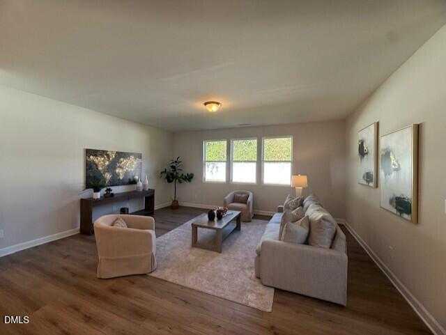 Cozy living room with beige sofa, armchairs, world map wall art, large windows, and hardwood floors in Davidson Homes The Preston C, Lillington, NC