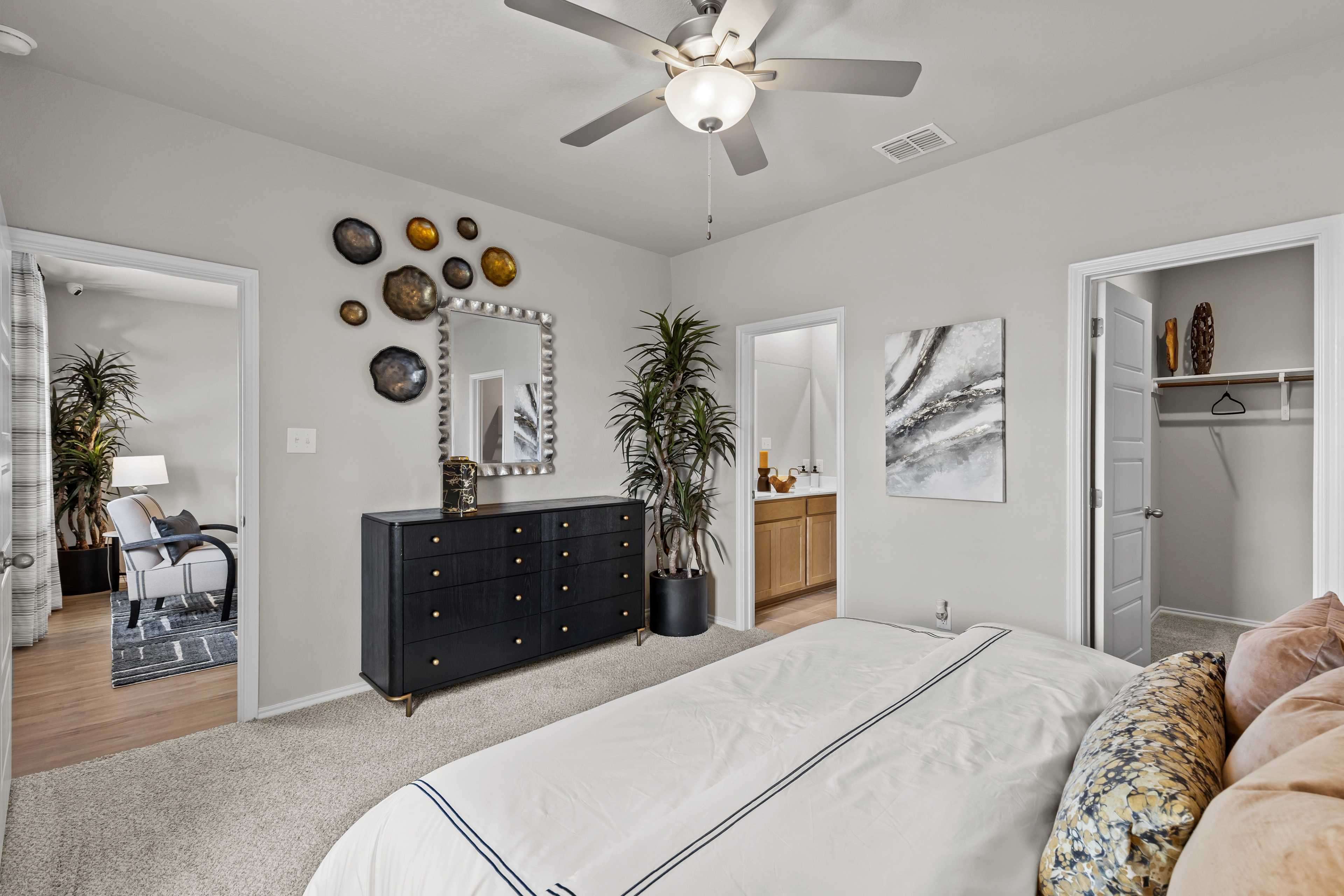 Spacious master bedroom in The Sabine C with king bed, black dresser, potted plants, ceiling fan, and en-suite bath access