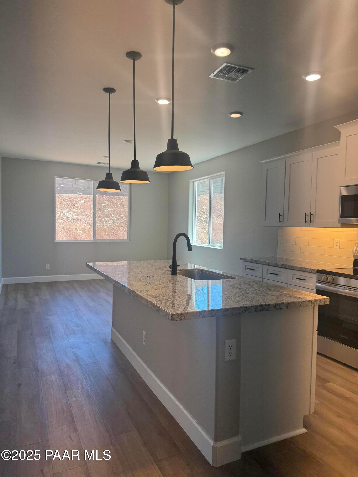 Modern kitchen with granite island, white cabinets, stainless appliances, pendant lights in The Summit B, Prescott Valley, AZ