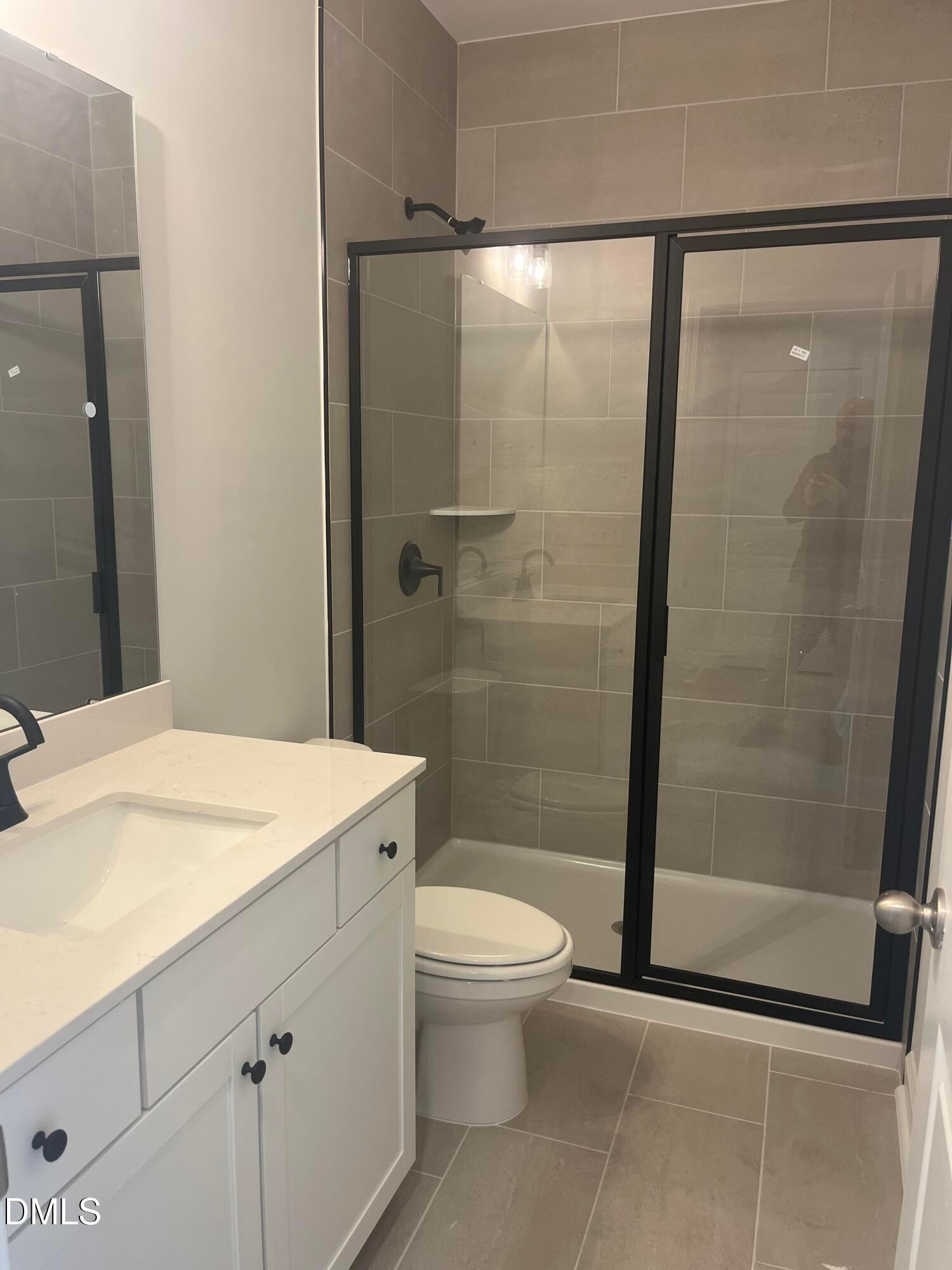 Modern primary bathroom with white quartz vanity, black-framed glass shower, gray tile in Davidson Homes The Birch II E, Wake Forest NC