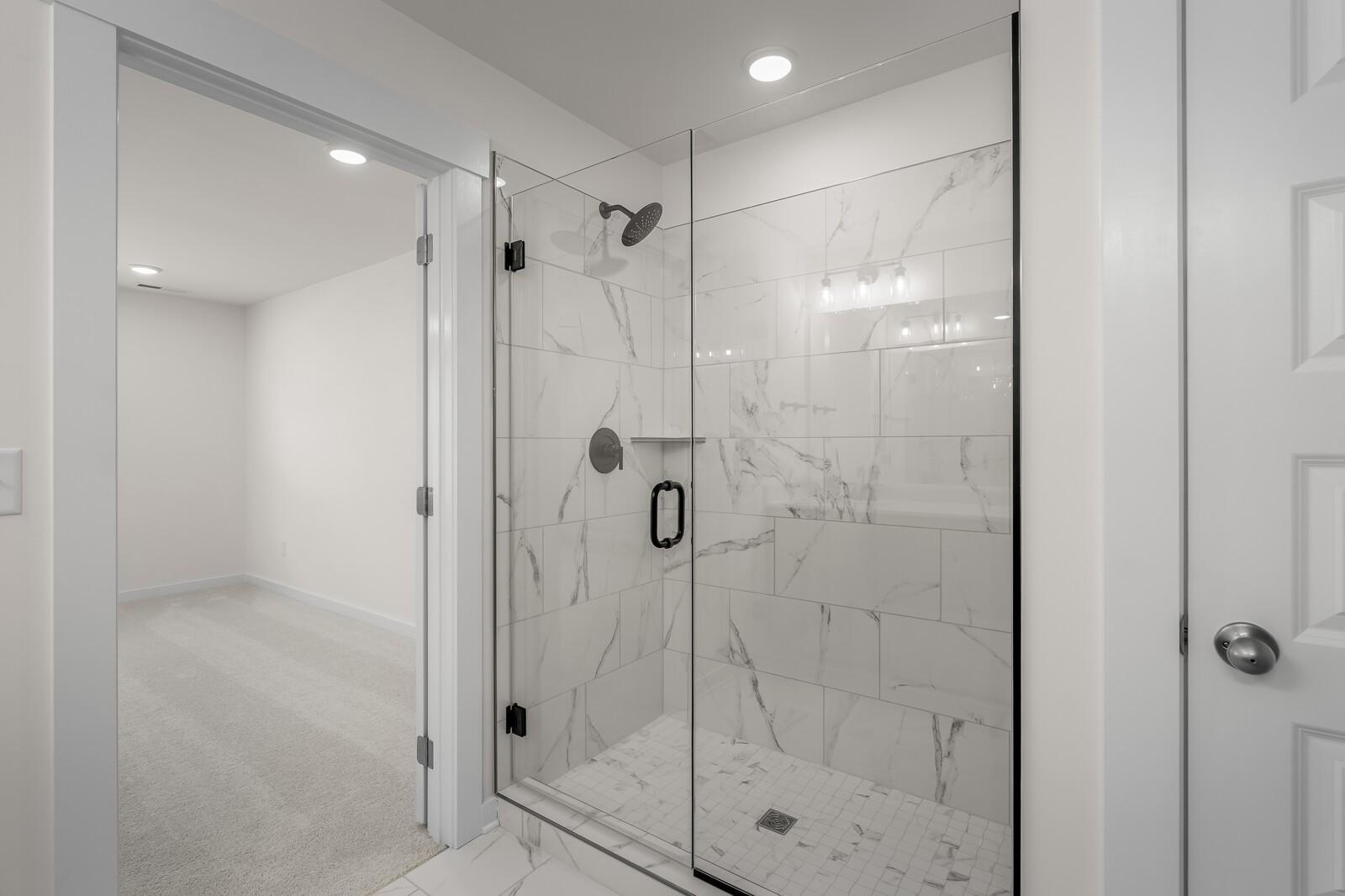 Modern walk-in shower with marble-look tile and glass door in The Willow home at Woods Crossing, Gallatin, Tennessee.