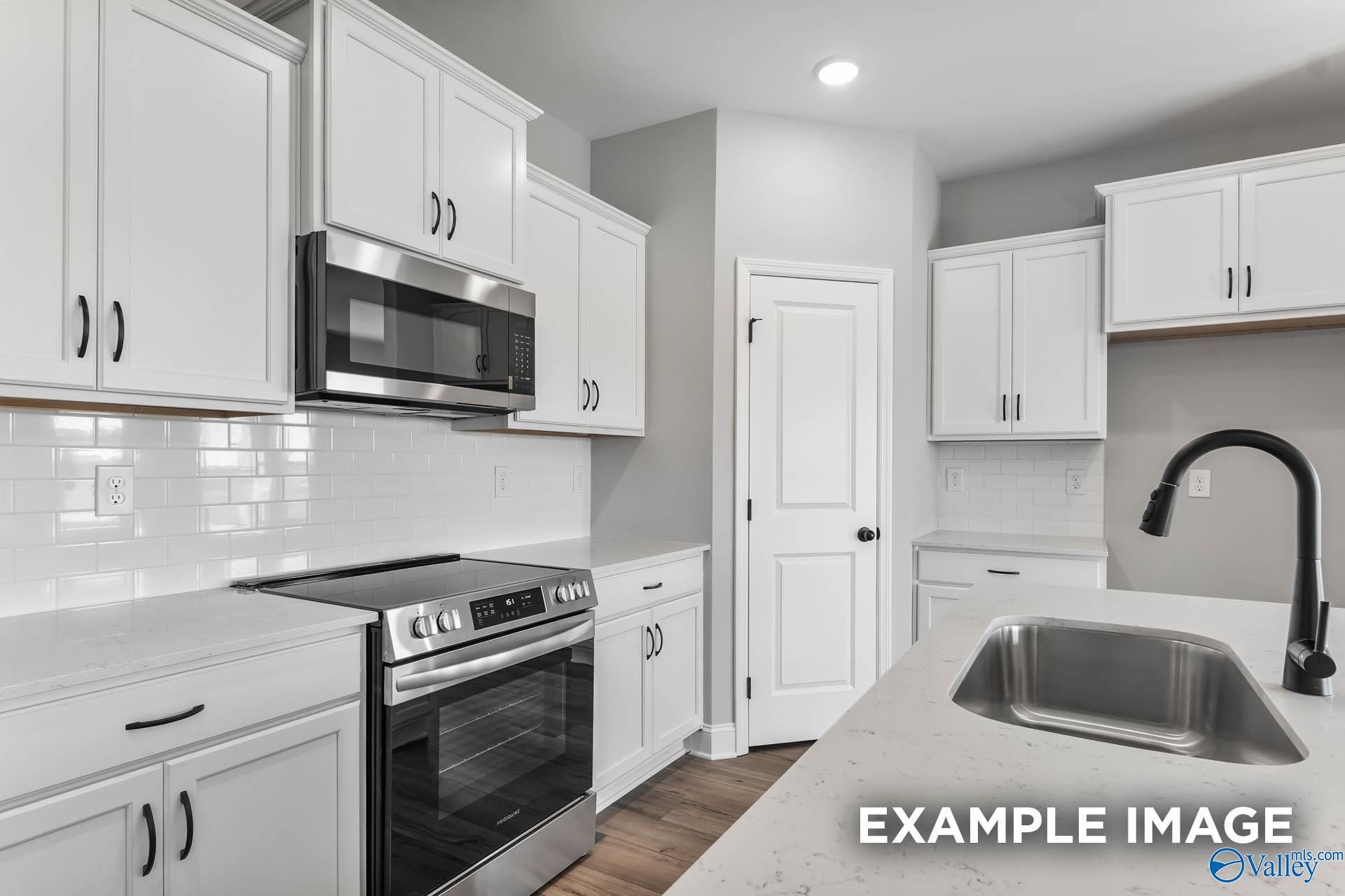 Modern white kitchen with stainless appliances, subway tile backsplash, and quartz island in The Daphne C 4-bed home, Athens, AL