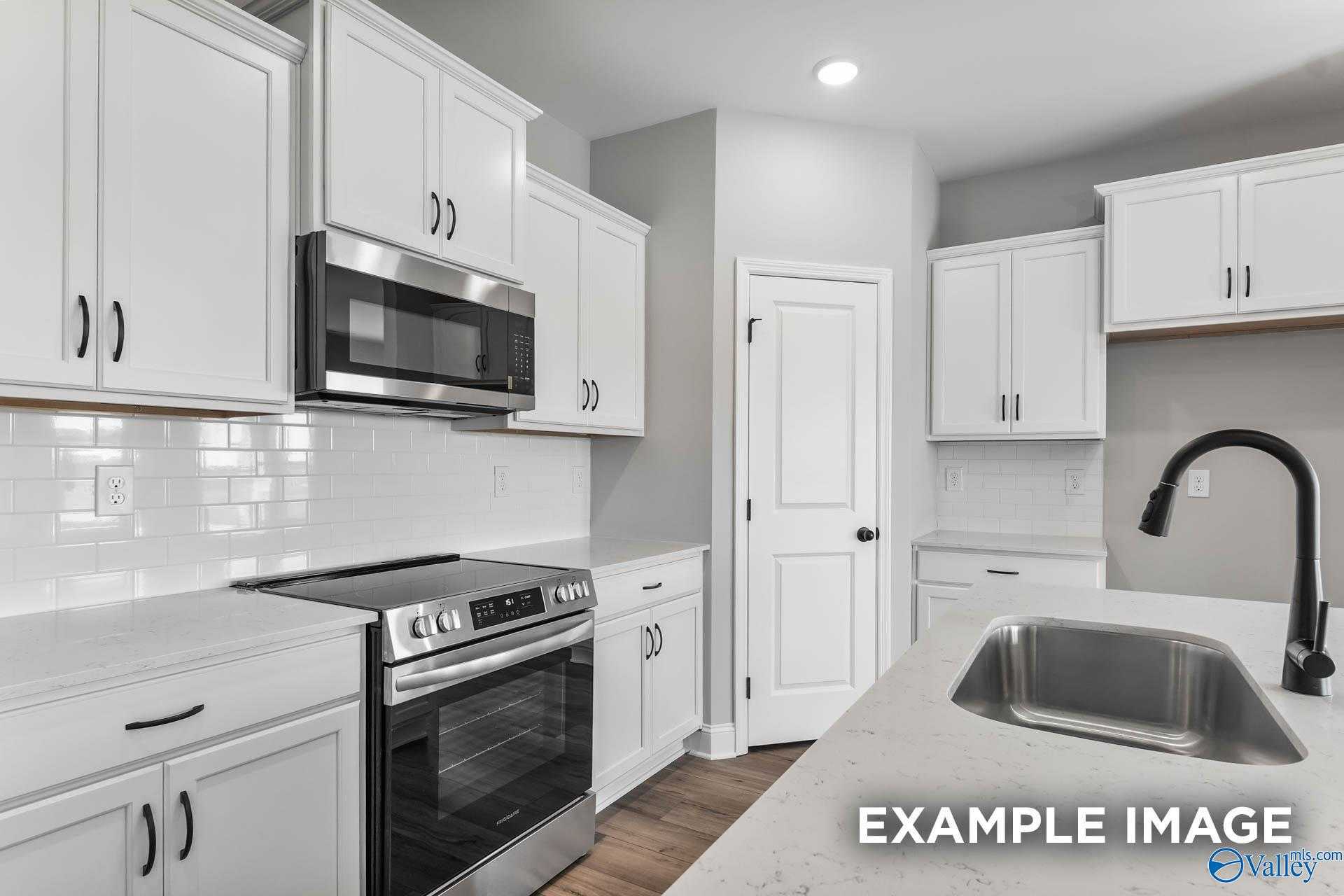 Modern white kitchen with stainless appliances, subway tile backsplash, and quartz island in The Daphne C 4-bed home, Athens, AL