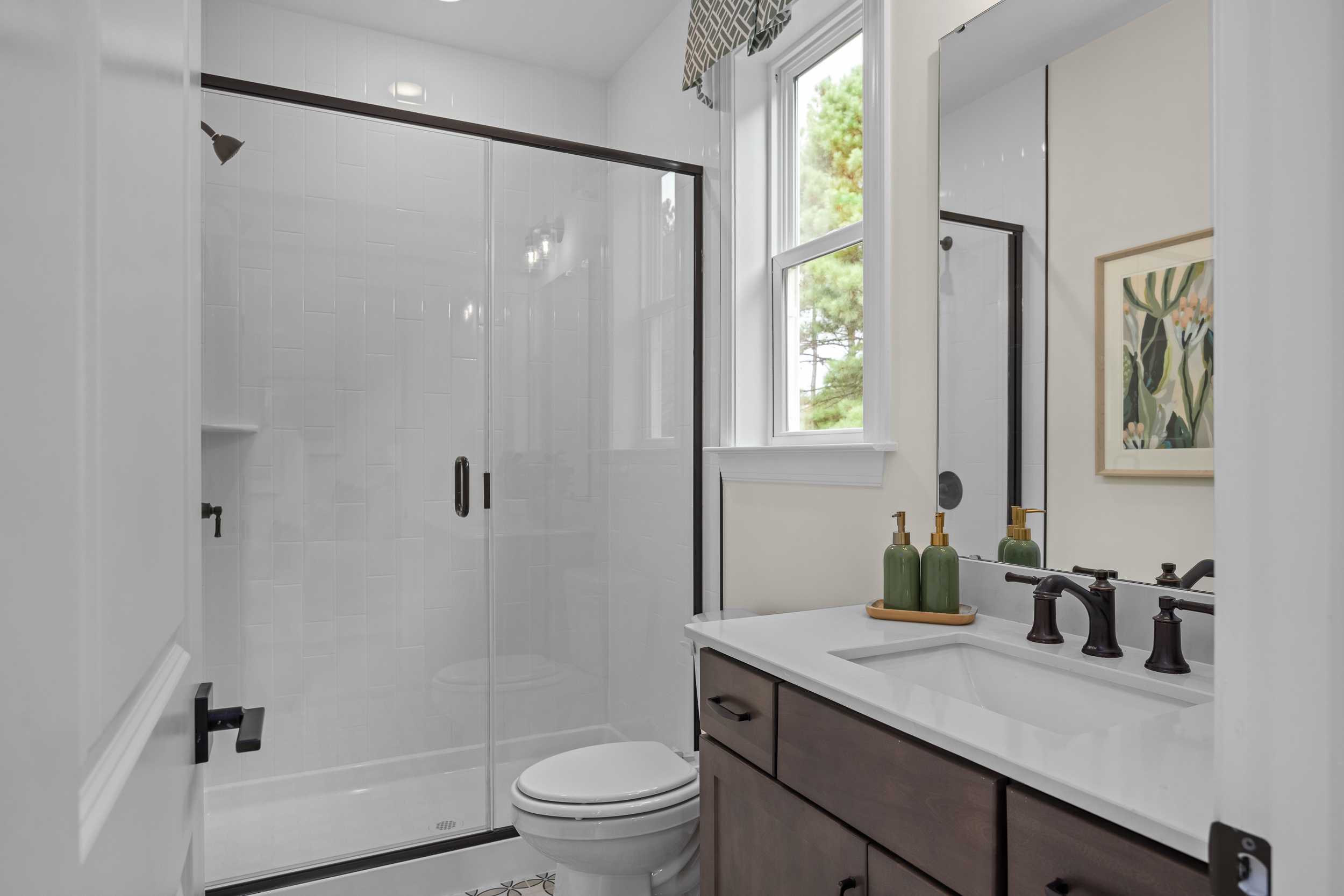 Elegant primary bathroom in Laneridge Estates Raleigh NC with glass shower, dark wood double vanity, and natural light
