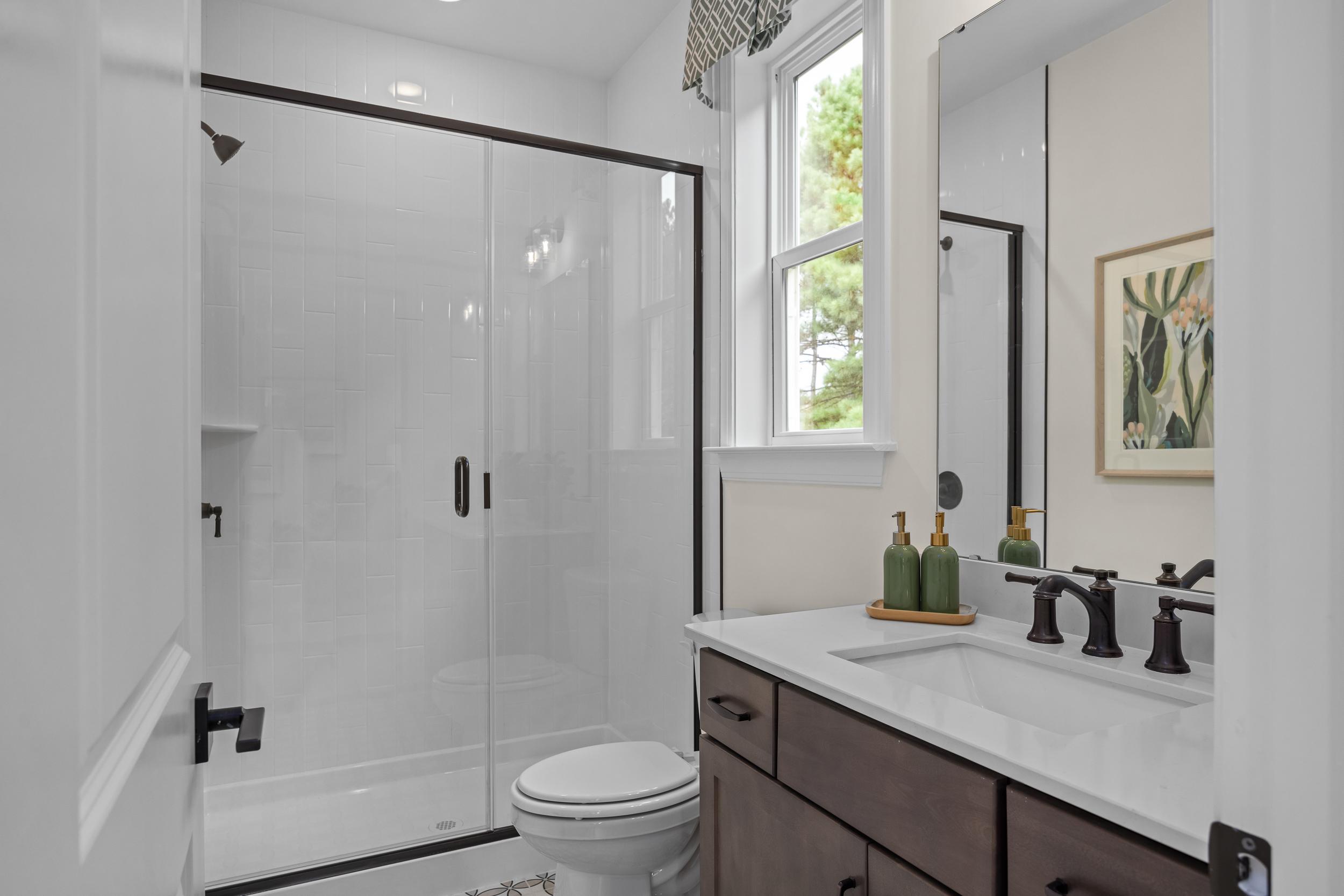 Elegant primary bathroom in Laneridge Estates Raleigh NC with glass shower, dark wood double vanity, and natural light
