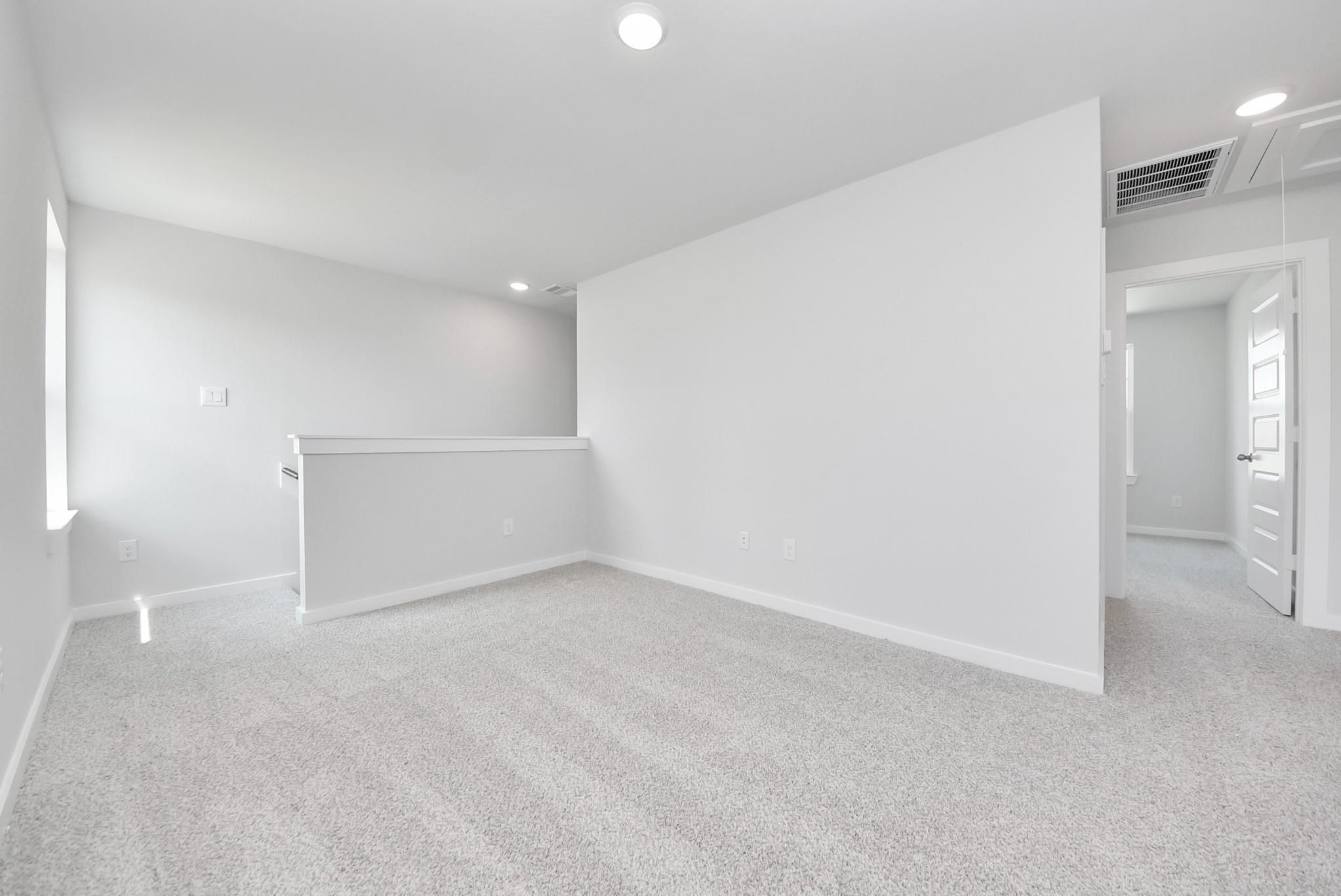 Bright, carpeted upstairs loft area in The Blanco F floor plan at Spring Branch Crossing in Conroe, Texas.