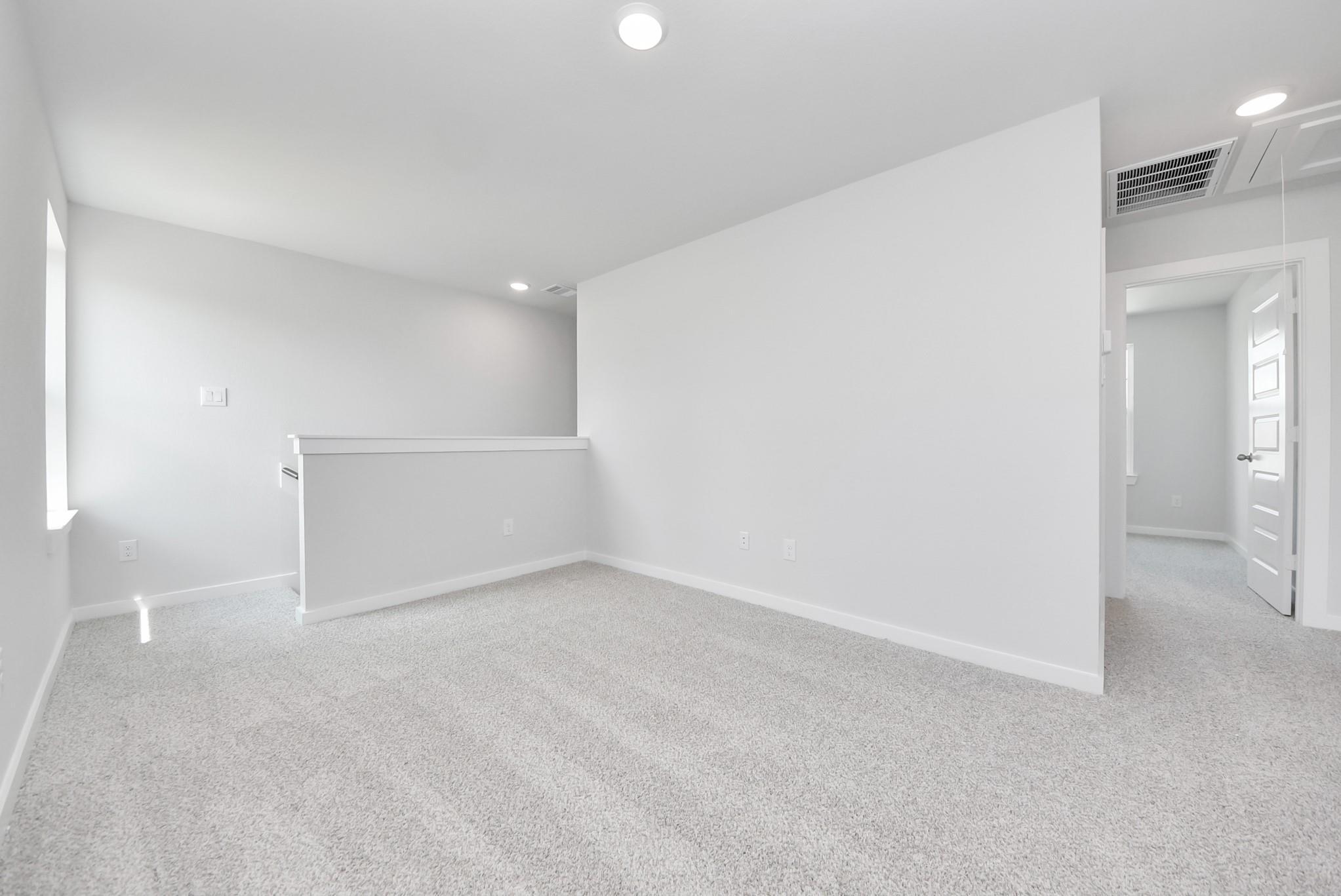 Bright, carpeted upstairs loft area in The Blanco F floor plan at Spring Branch Crossing in Conroe, Texas.