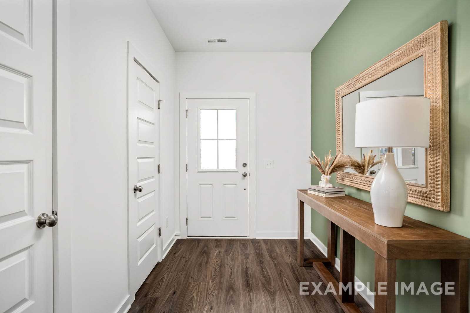 Spacious entryway in The Gordon B home with green accent wall, ornate mirror, wooden console table, lamp, and hardwood floors
