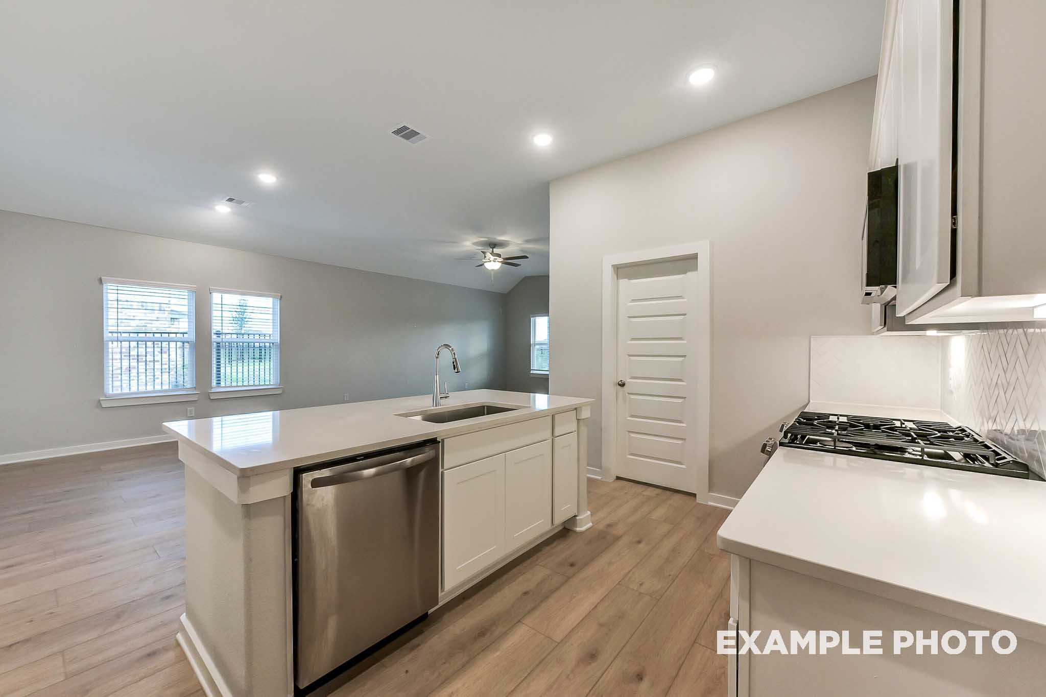 Modern kitchen in The Laguna B showcasing white shaker cabinets, quartz island with sink, stainless steel dishwasher, gas cooktop, and open living space